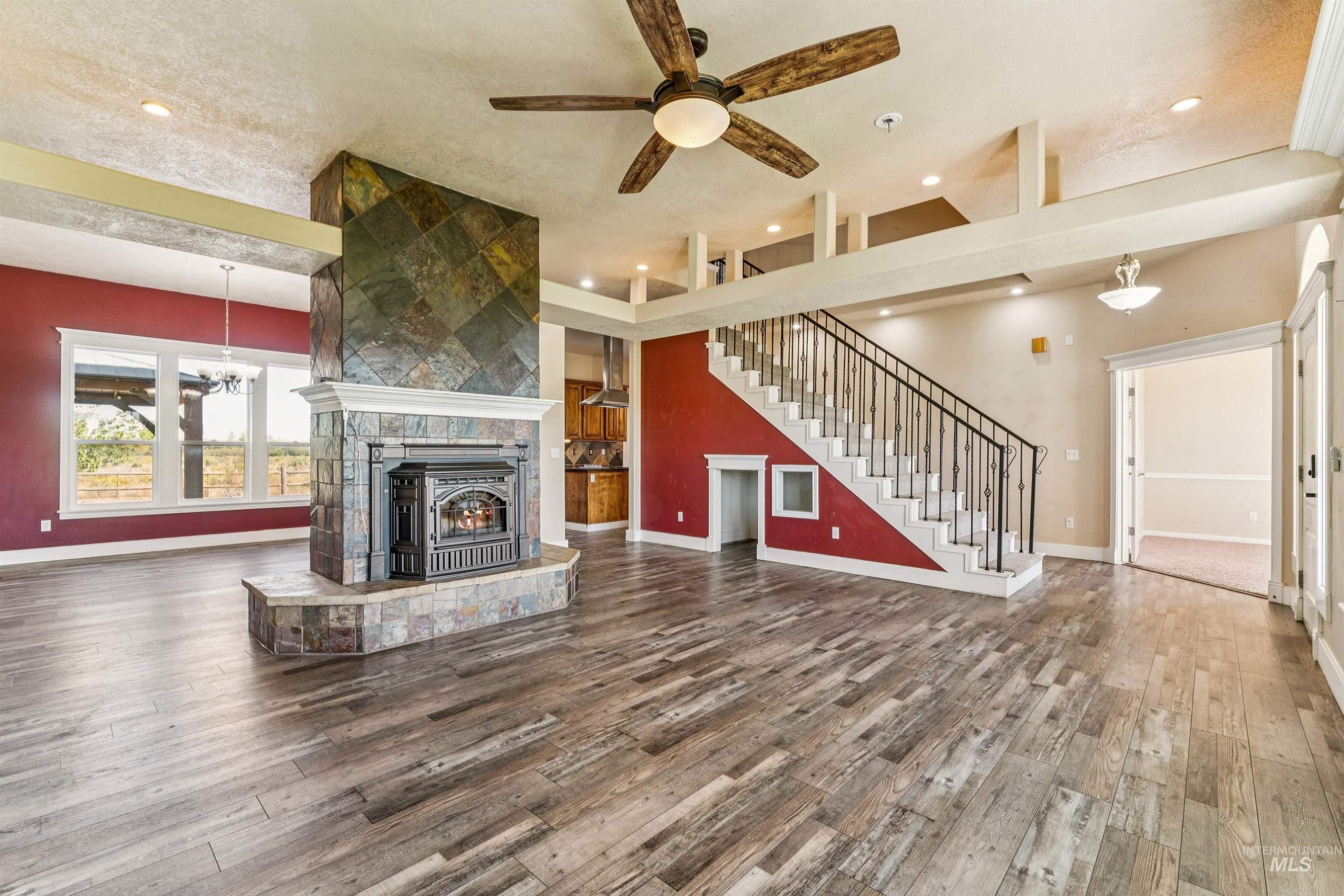 Unfurnished living room with dark wood-type flooring, a tiled fireplace, recessed lighting, a chandelier, and ceiling fan