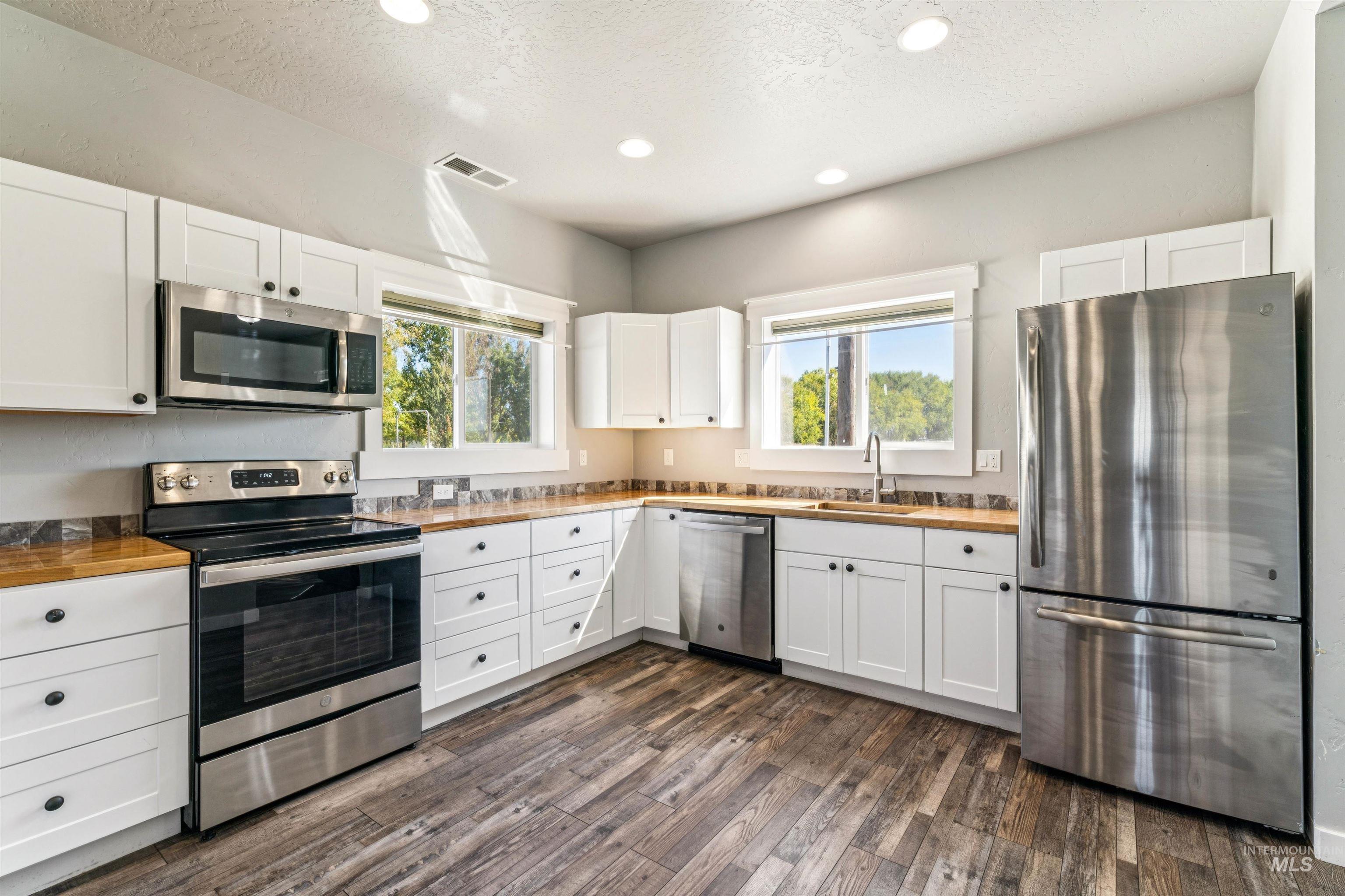 Kitchen with stainless steel appliances, a textured ceiling, white cabinetry, plenty of natural light, and dark wood-style floors