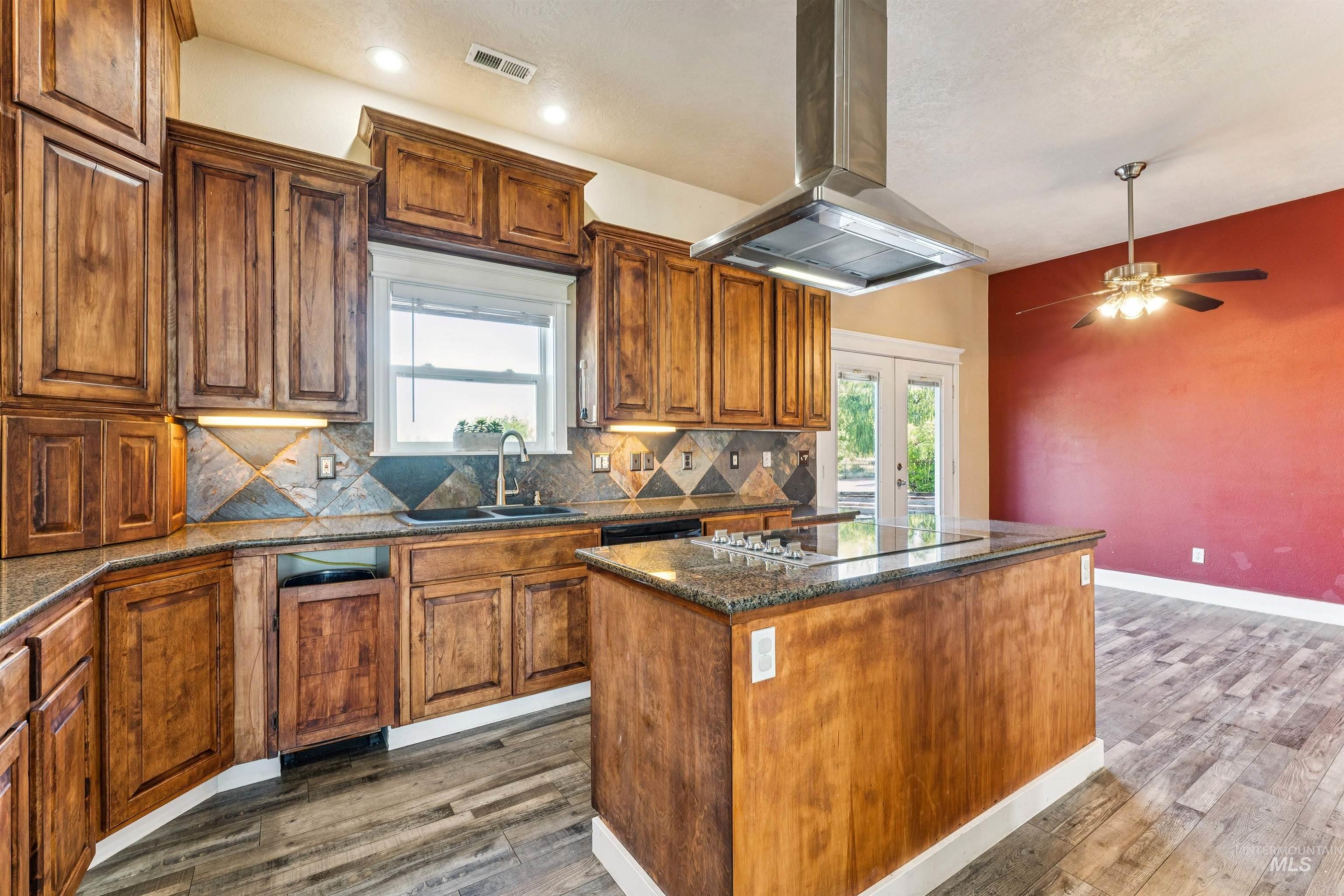 Kitchen featuring dark stone countertops, french doors, island exhaust hood, backsplash, and a kitchen island