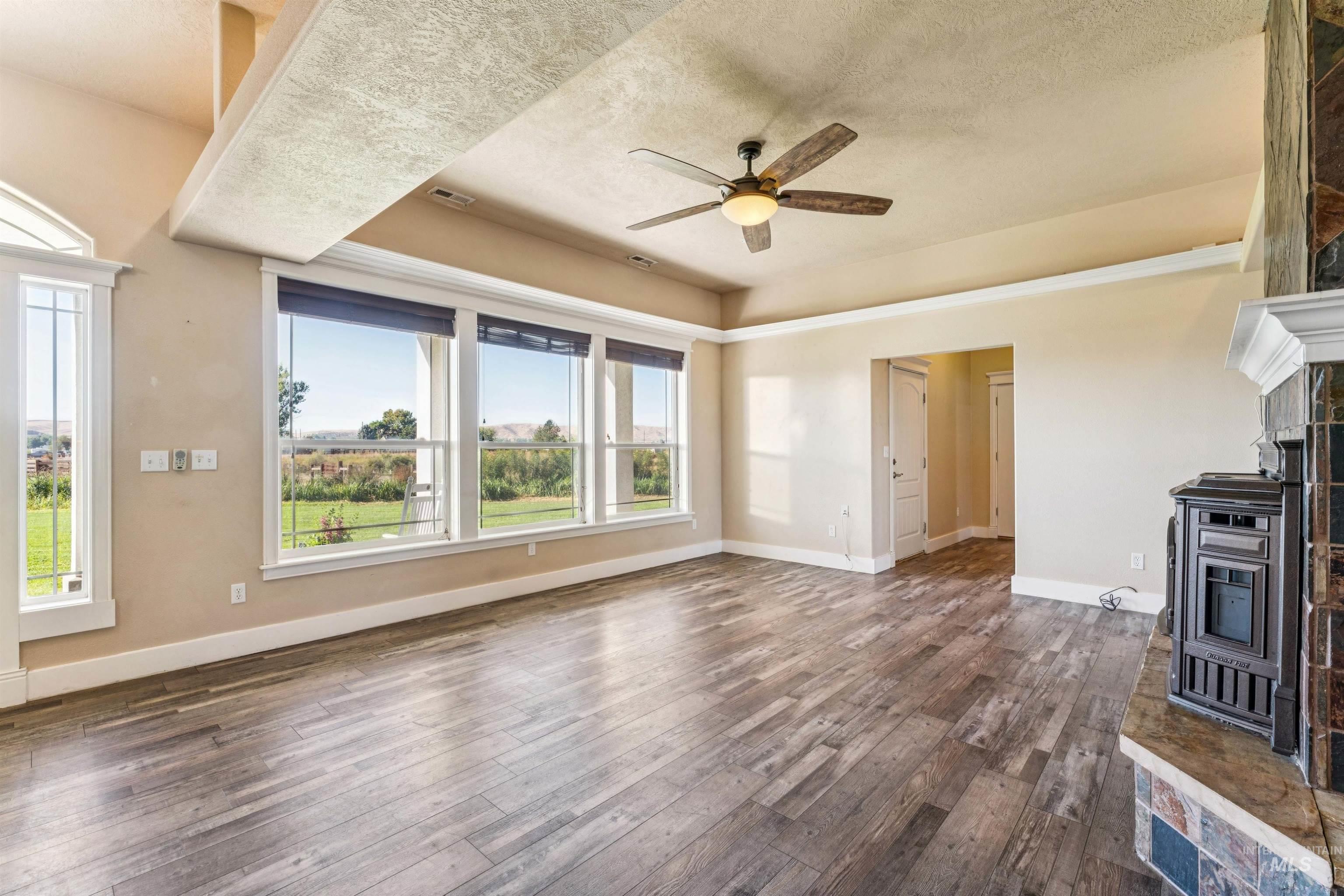 Unfurnished living room with a fireplace, a raised ceiling, dark wood-style flooring, ceiling fan, and a textured ceiling