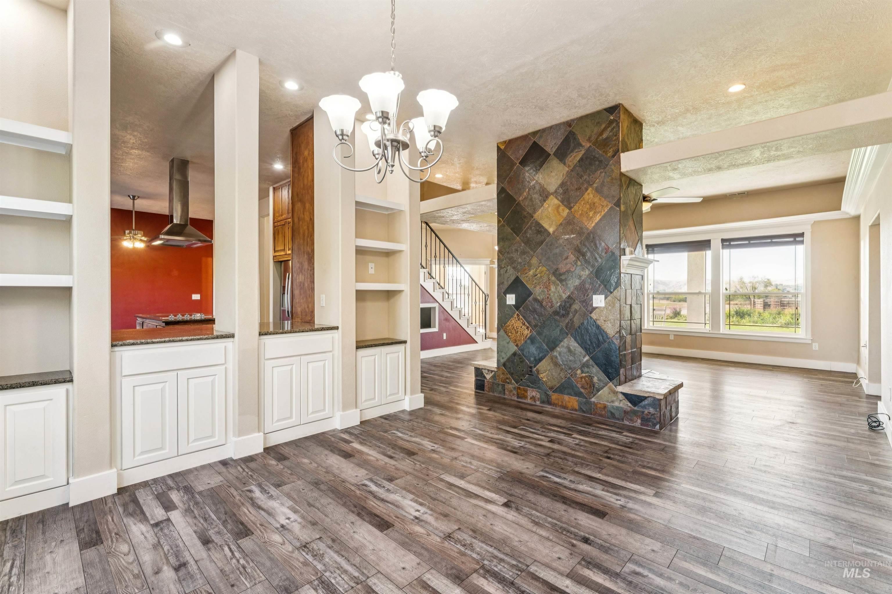 Unfurnished living room featuring a ceiling fan, dark wood-style floors, built in shelves, a chandelier, and a textured ceiling