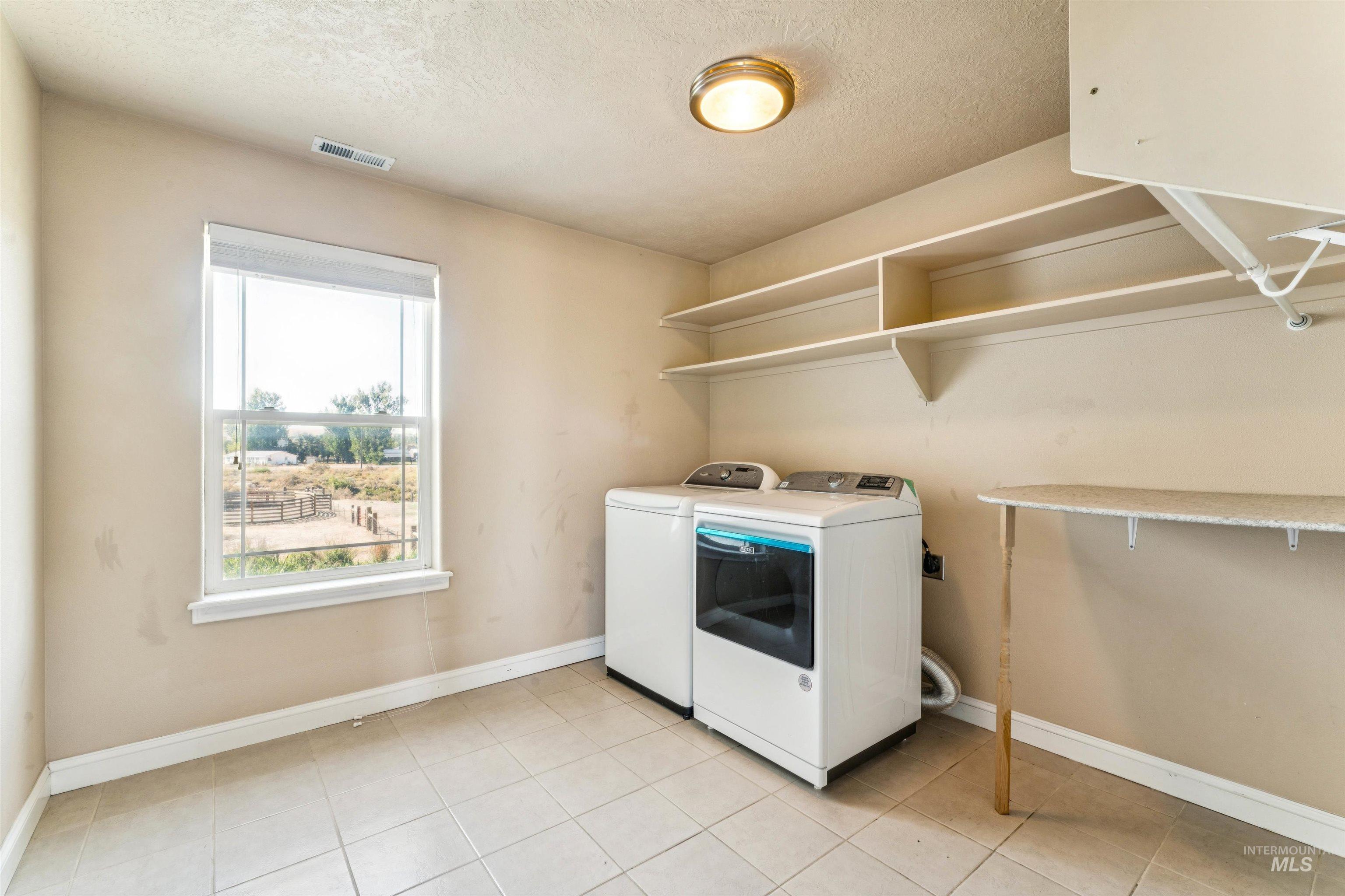 Washroom with a textured ceiling, washer and clothes dryer, and light tile patterned flooring