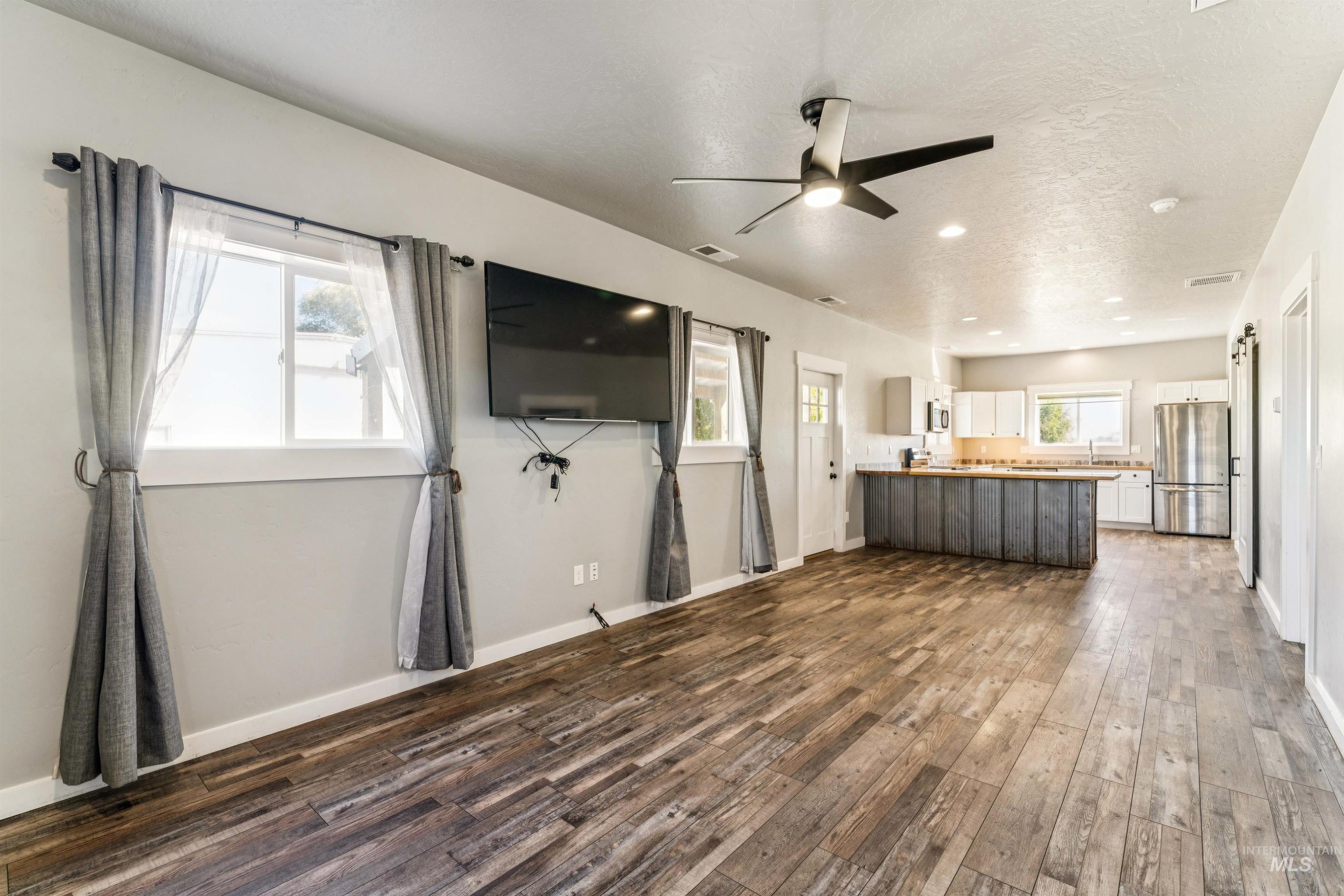 Unfurnished living room featuring dark wood-style flooring, a textured ceiling, and a ceiling fan