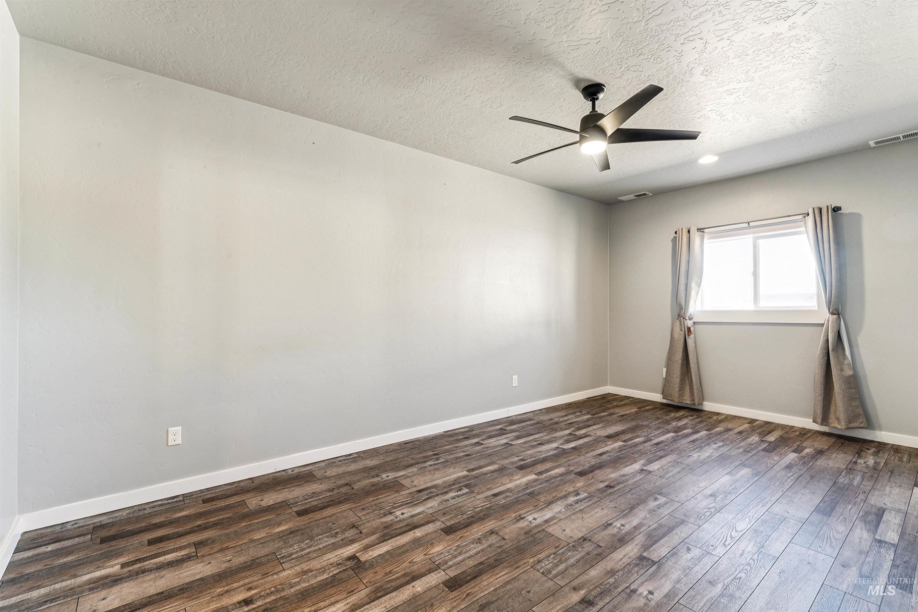 Unfurnished room with a textured ceiling, dark wood finished floors, and a ceiling fan