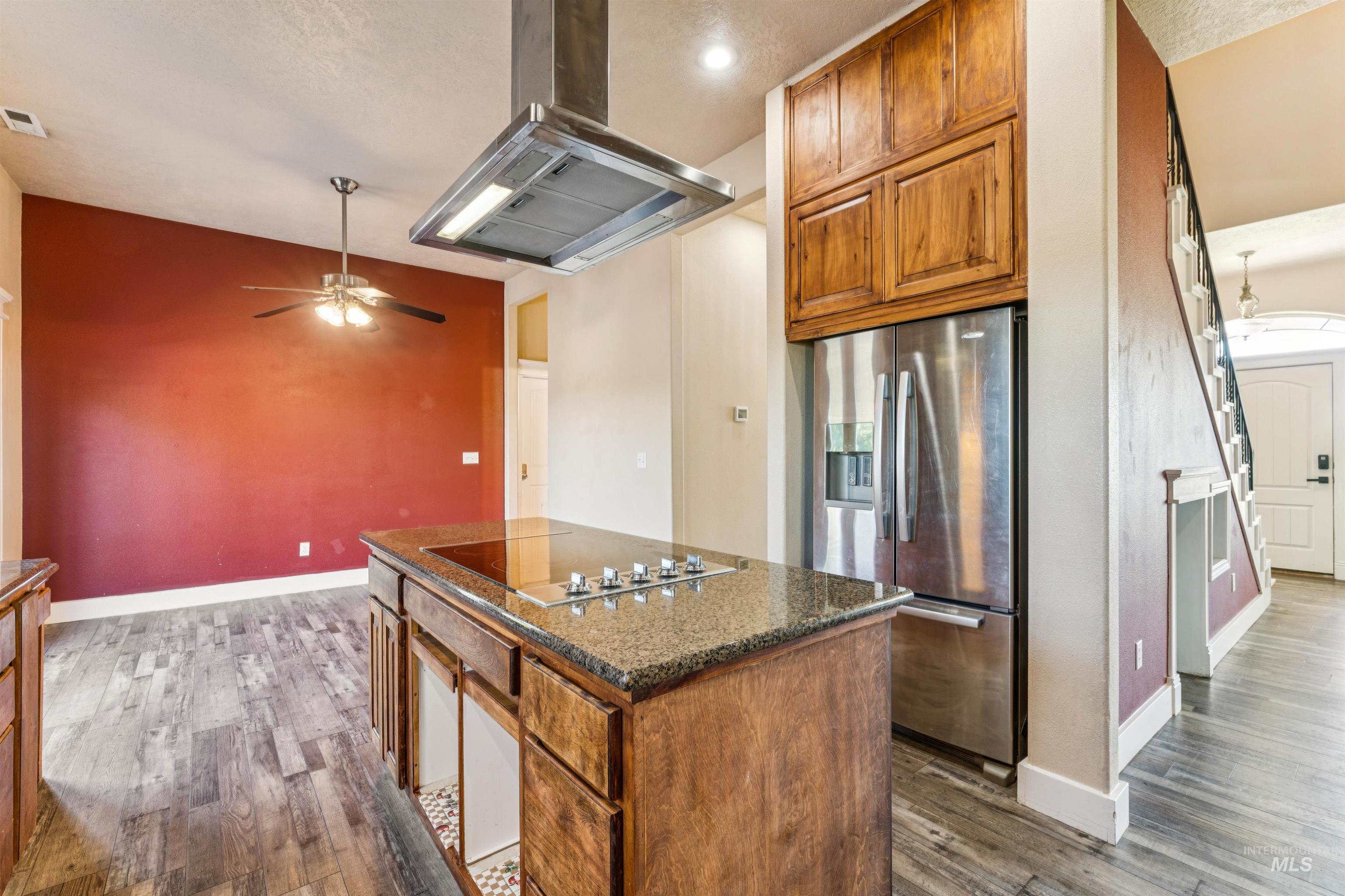 Kitchen featuring brown cabinets, stainless steel refrigerator with ice dispenser, ventilation hood, a kitchen island, and dark wood-type flooring