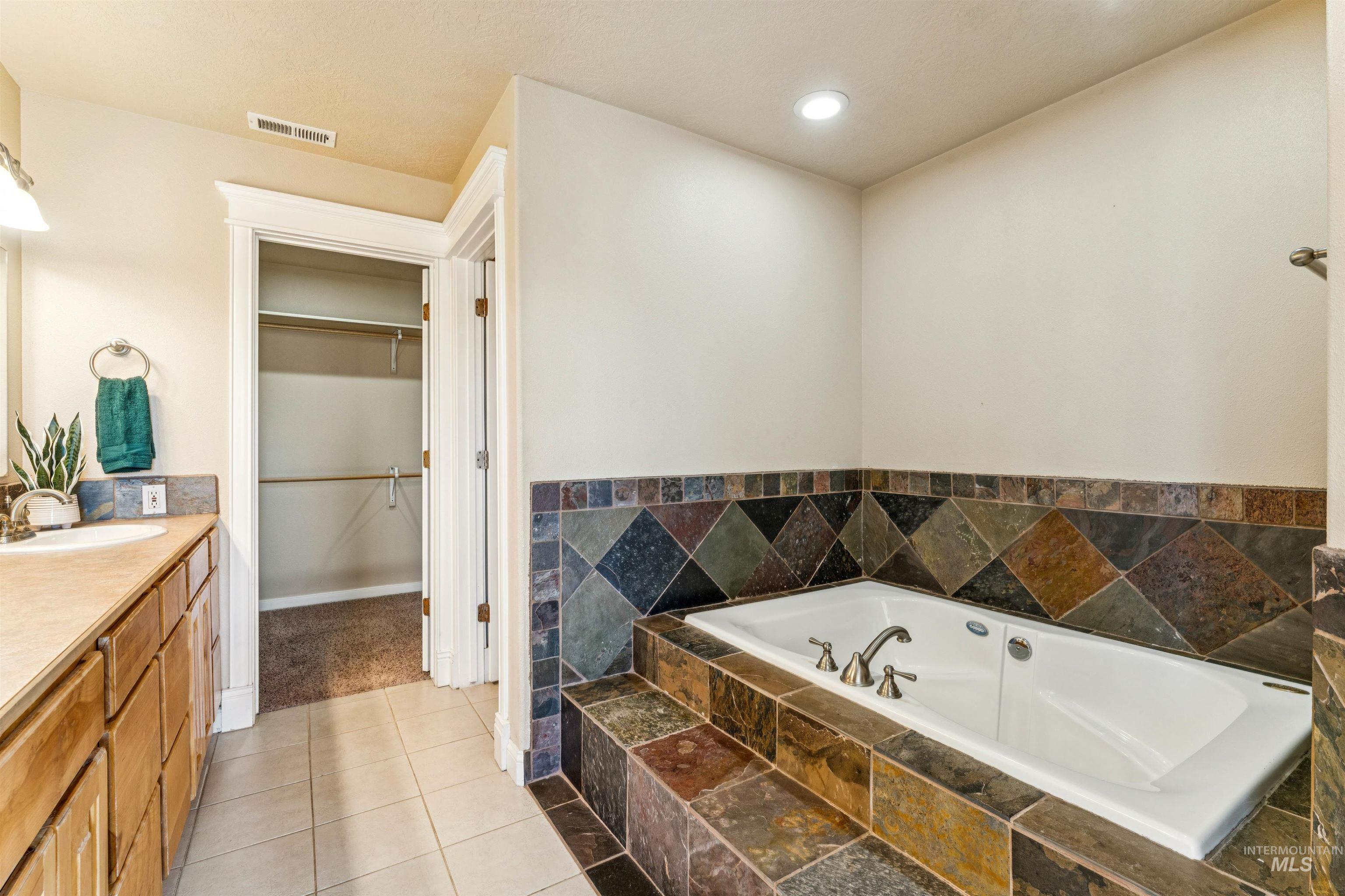 Full bathroom featuring vanity, a garden tub, a walk in closet, light tile patterned floors, and recessed lighting