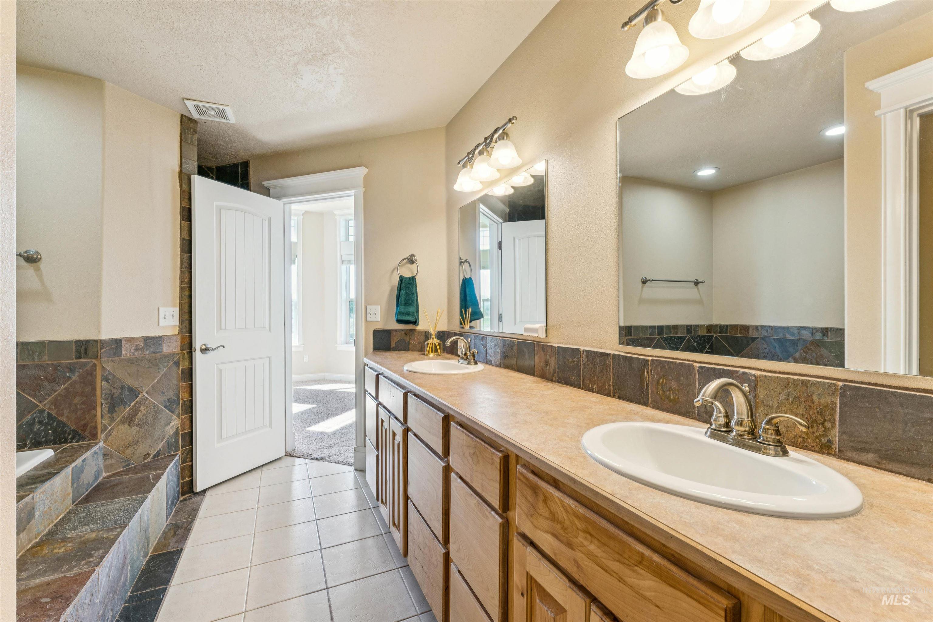 Full bathroom with light tile patterned flooring, double vanity, and a bath