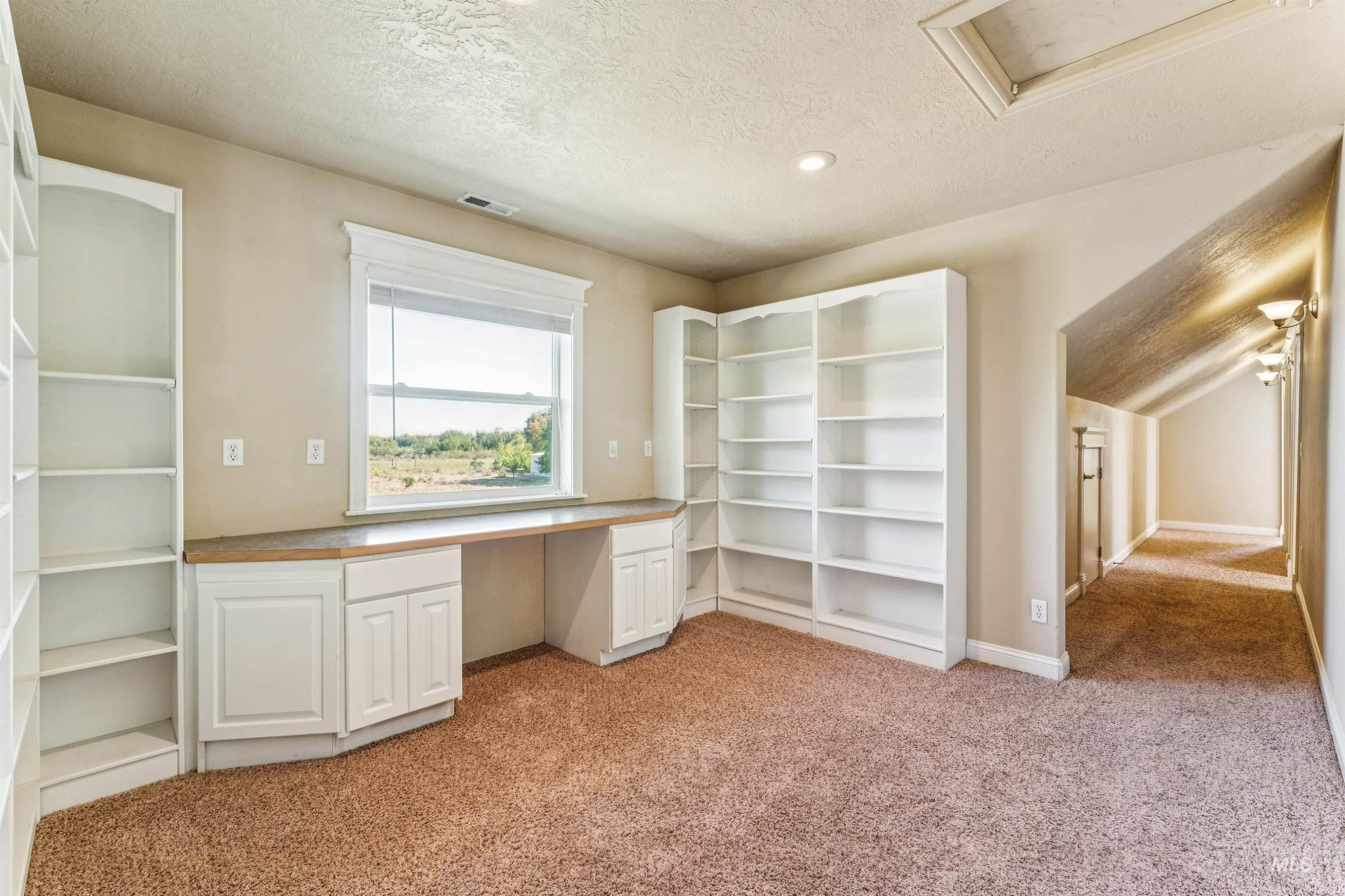 Unfurnished office with light colored carpet, built in study area, a textured ceiling, and attic access