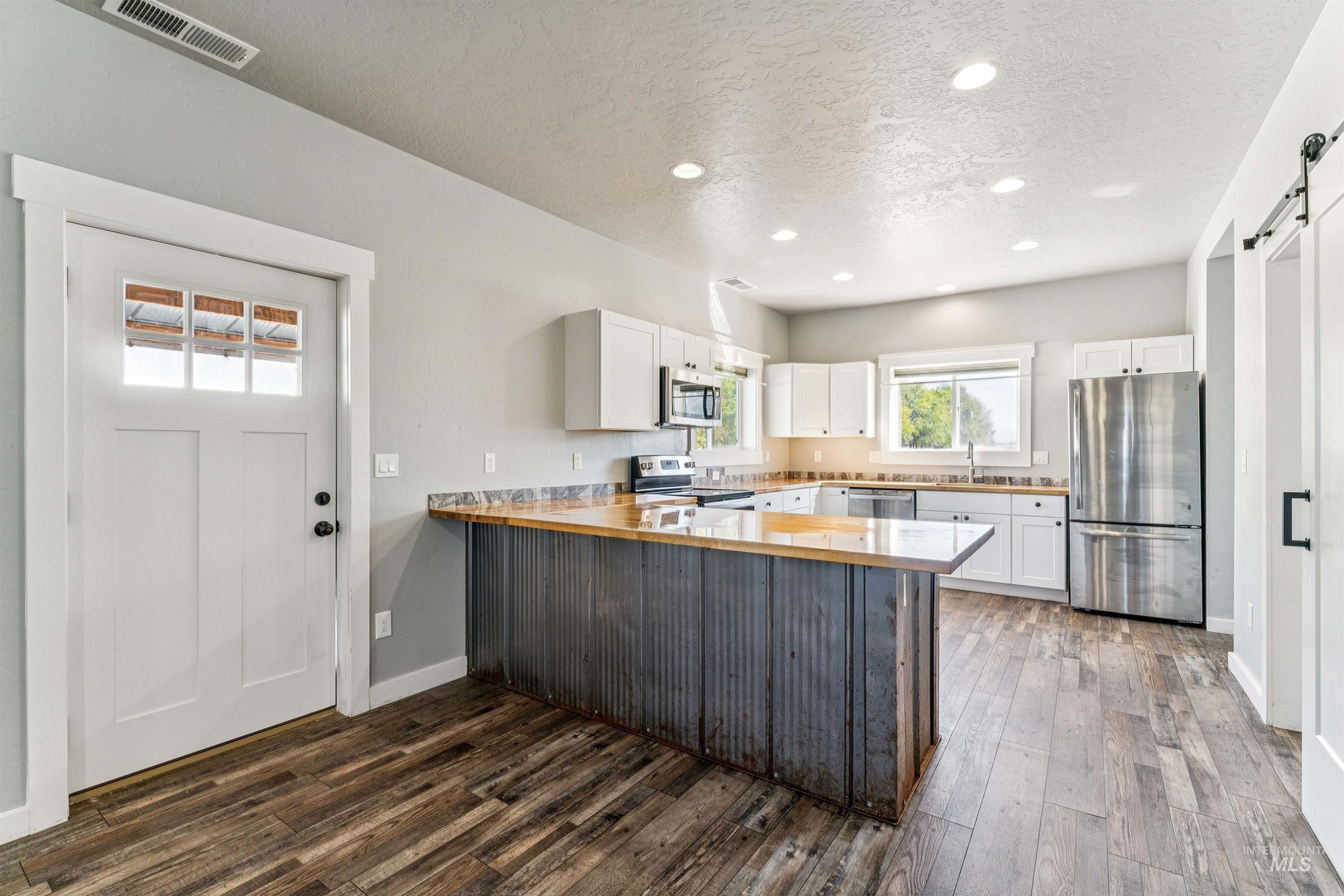 Kitchen featuring a barn door, white cabinetry, appliances with stainless steel finishes, a peninsula, and recessed lighting