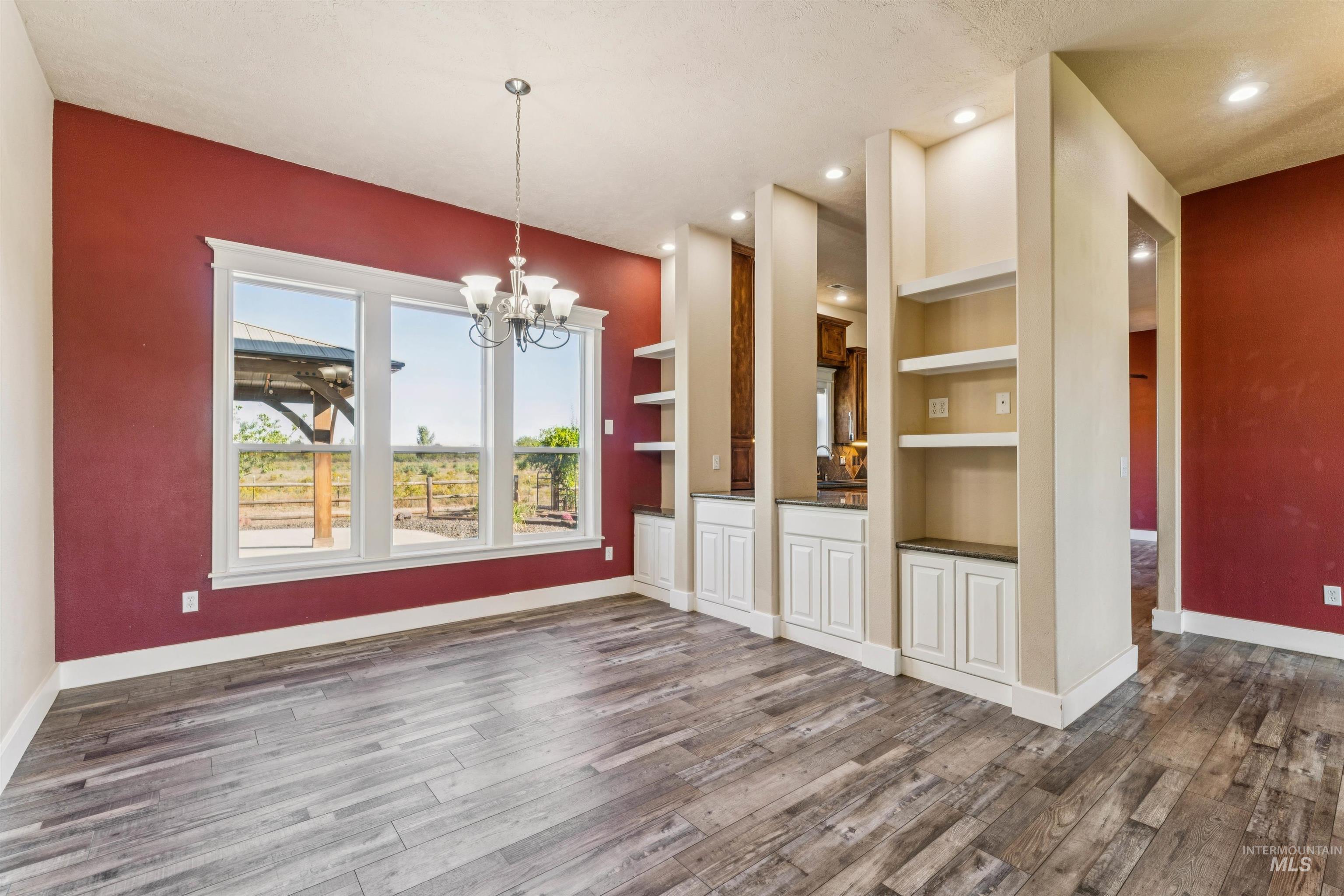 Unfurnished dining area with built in shelves, a chandelier, dark wood-style flooring, and recessed lighting