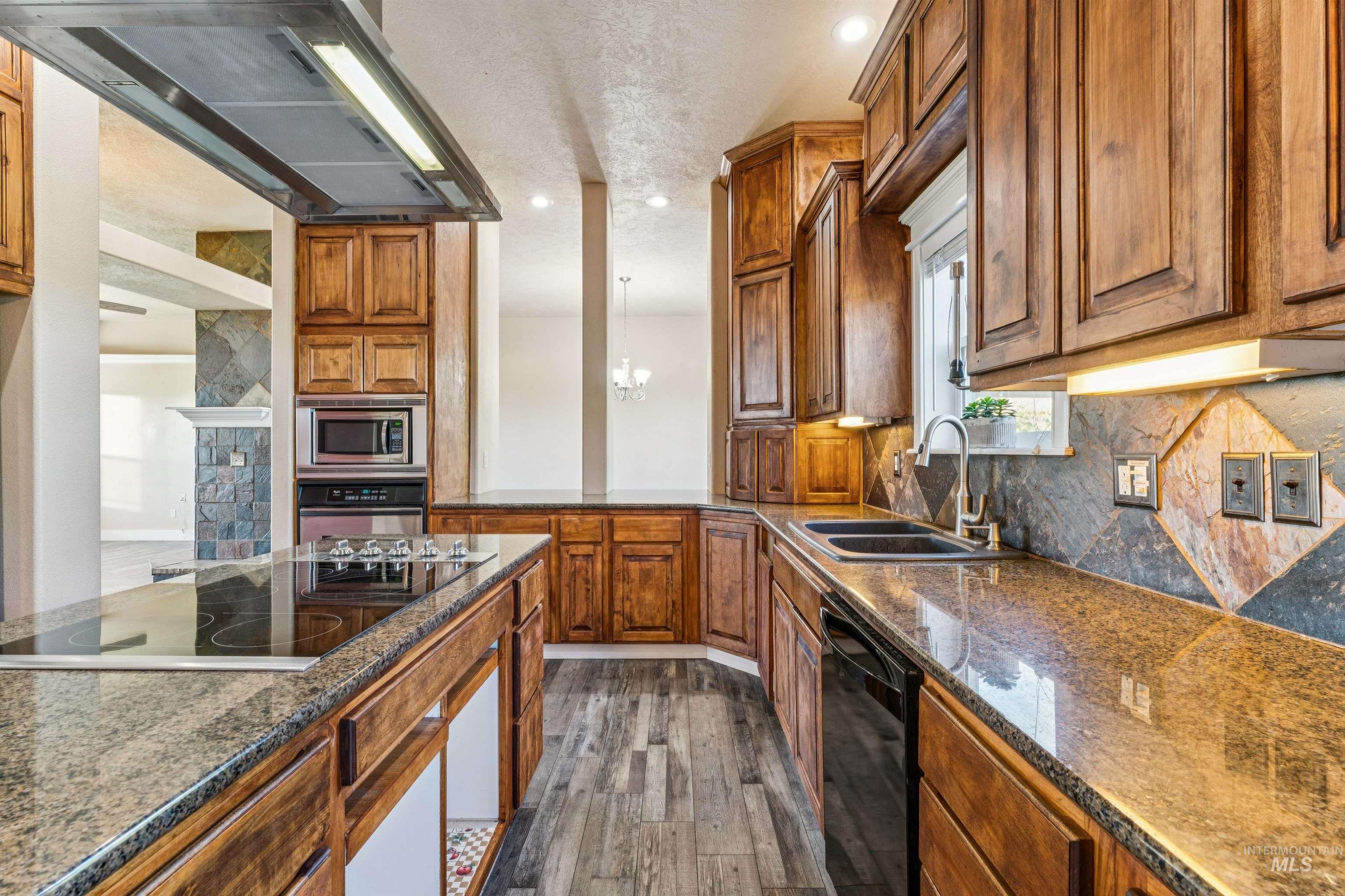 Kitchen featuring ventilation hood, brown cabinets, black appliances, dark wood-style floors, and dark stone countertops