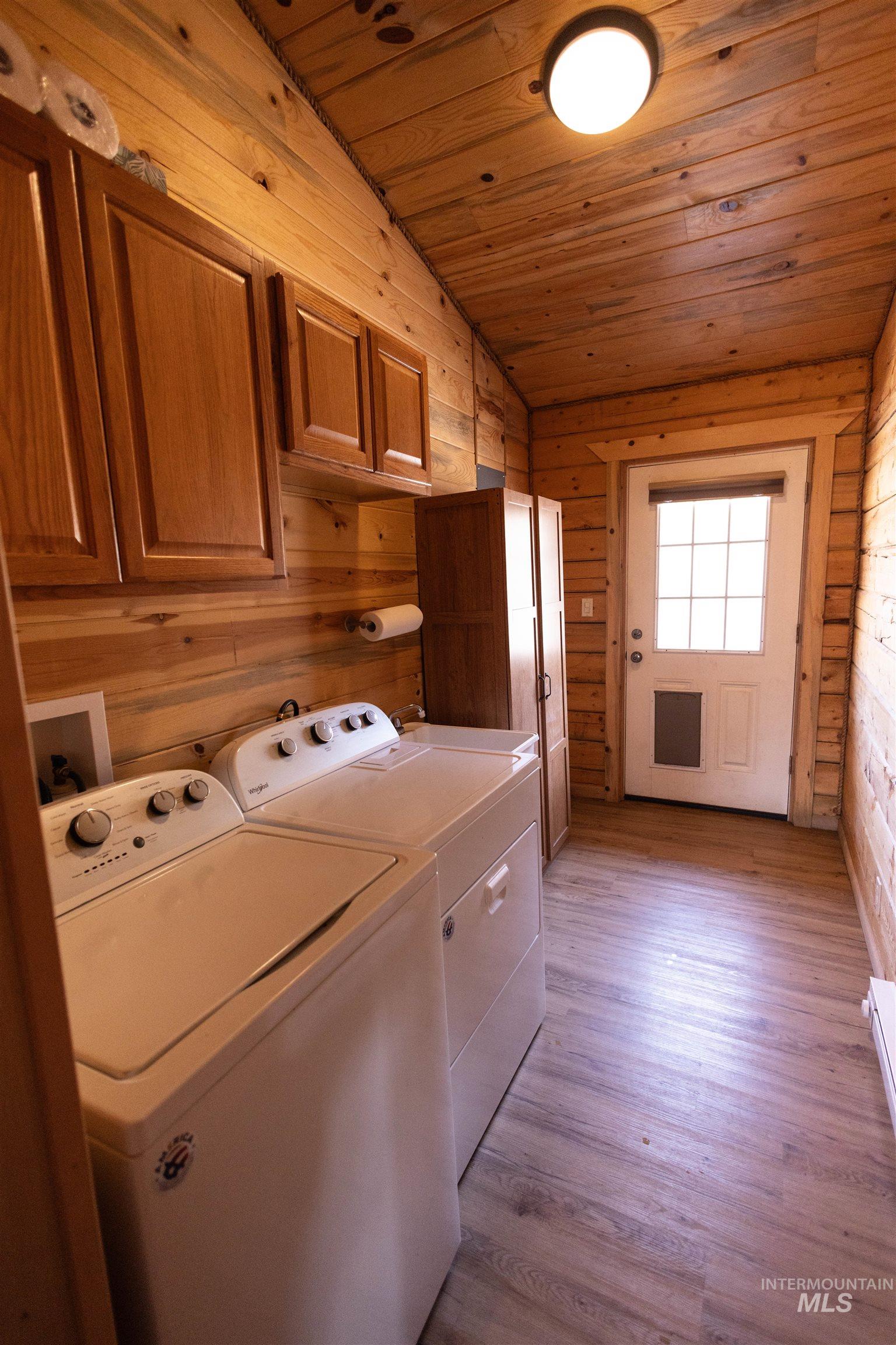 Laundry room featuring wood walls, light wood finished floors, wood ceiling, cabinet space, and washer and clothes dryer