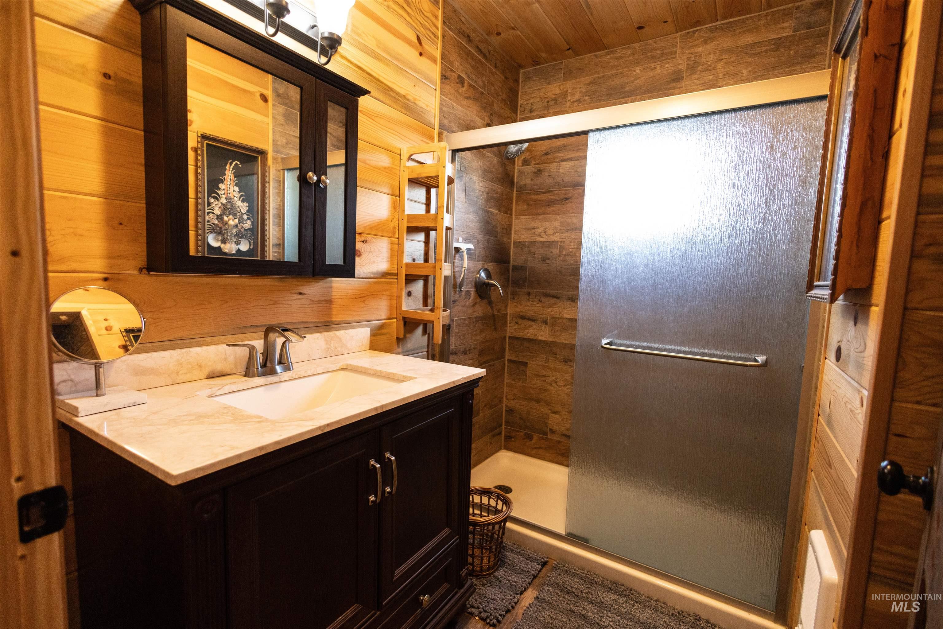 Full bath featuring vanity, a shower stall, wood walls, and wood ceiling