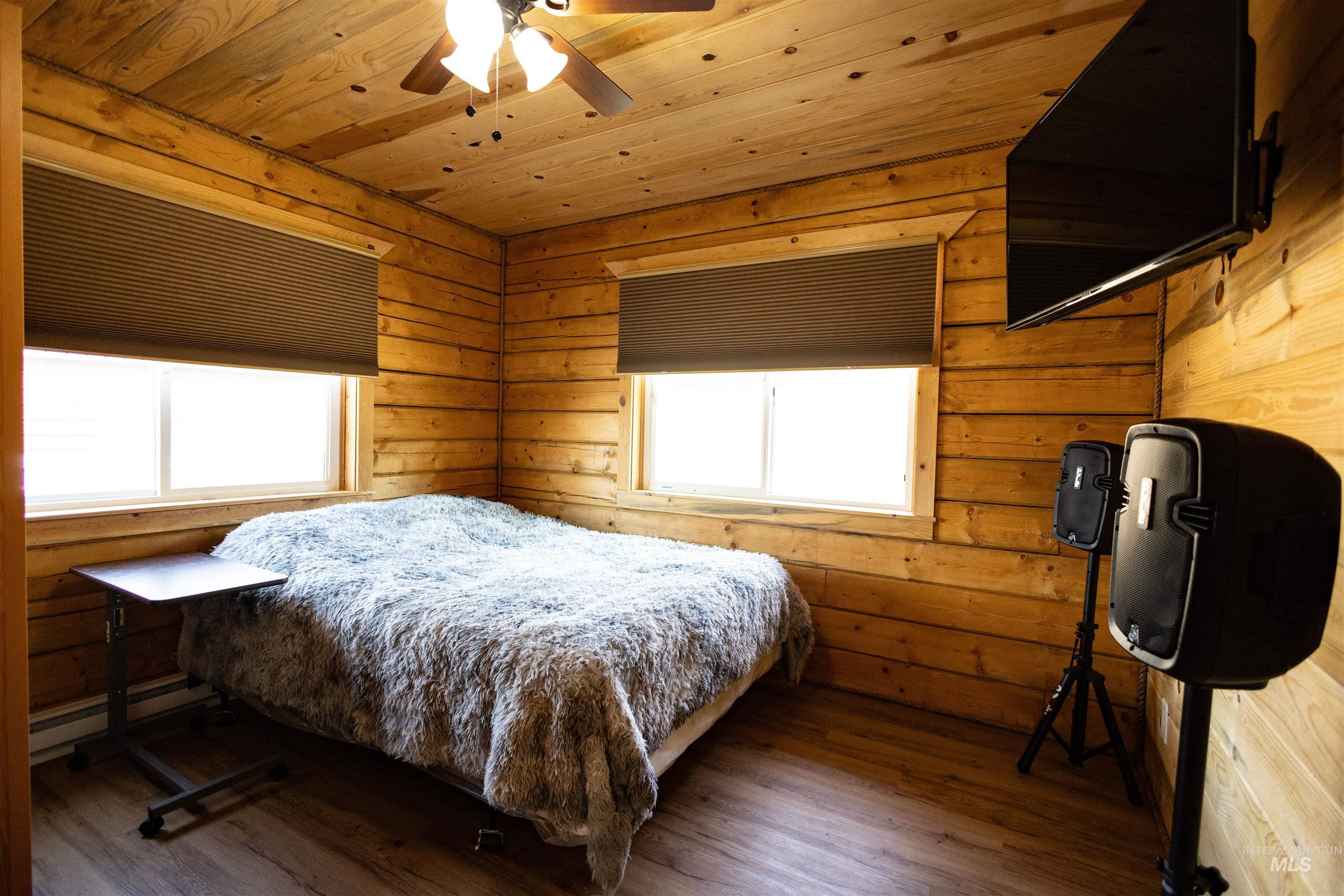Bedroom featuring wood ceiling, wood finished floors, wood walls, a baseboard radiator, and ceiling fan