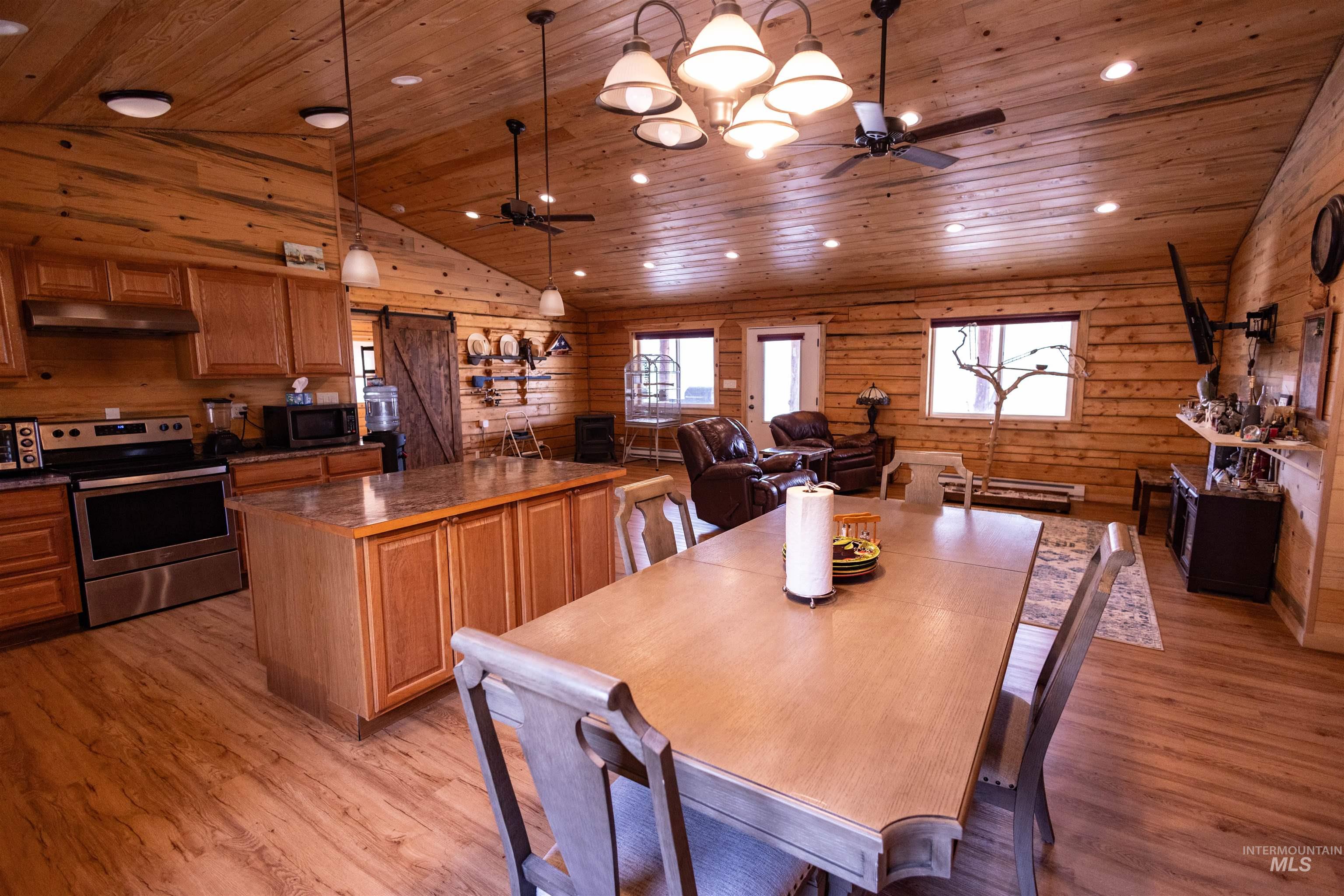 Dining space with wood ceiling, light wood-type flooring, wood walls, a ceiling fan, and a barn door