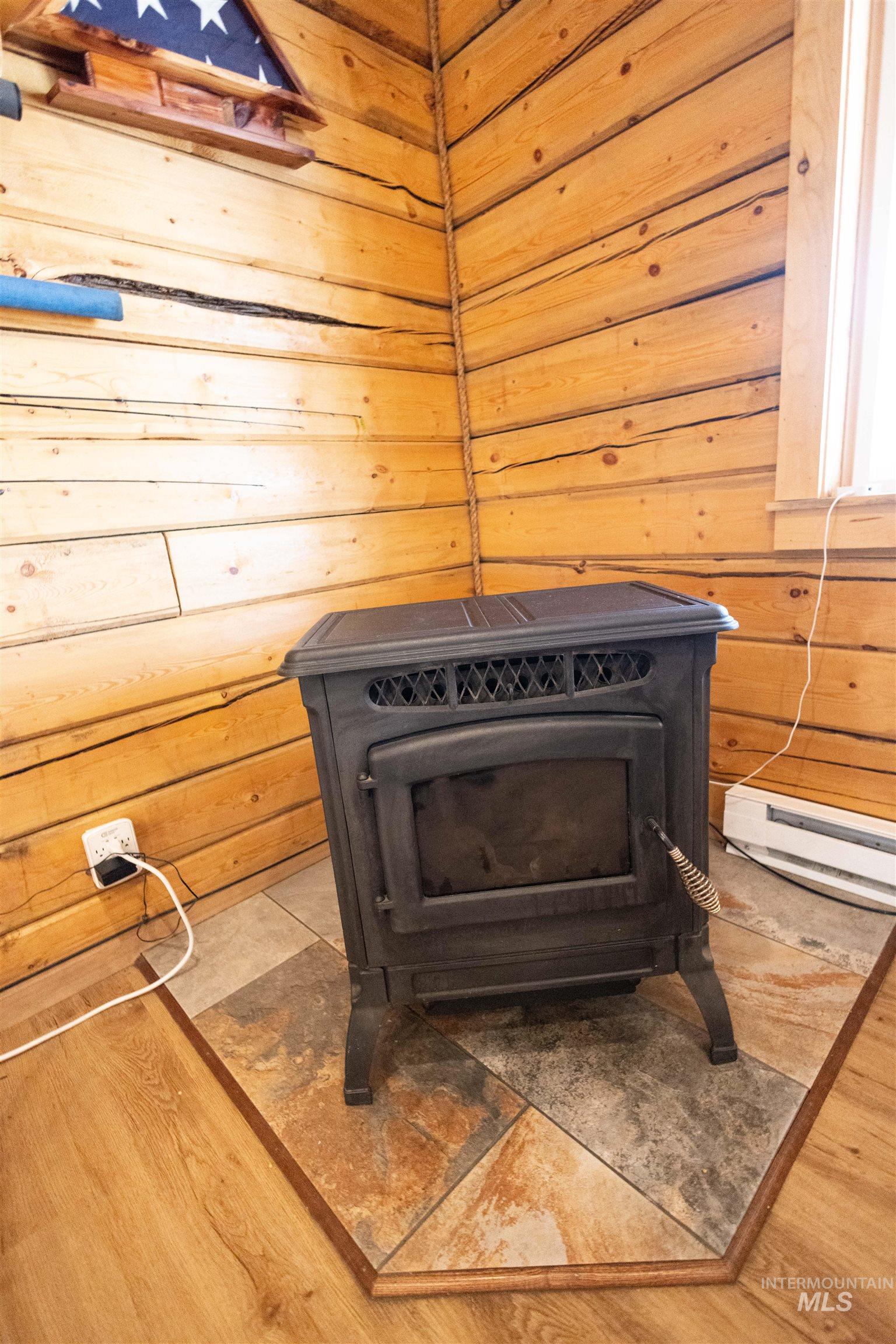 Detailed view of wooden walls, a wood stove, a baseboard radiator, and wood finished floors