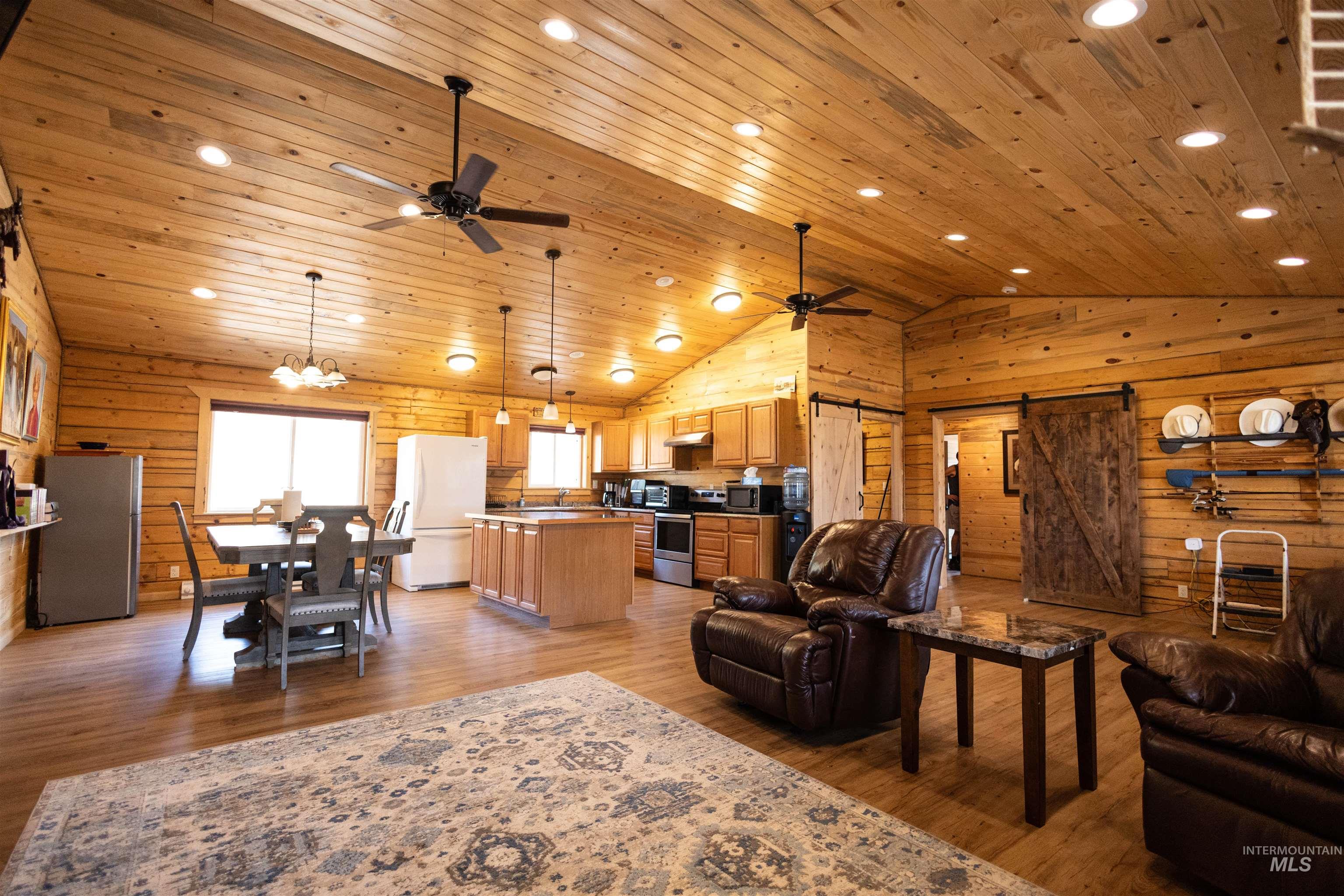 Living area with a barn door, light wood-type flooring, wooden ceiling, ceiling fan, and wooden walls