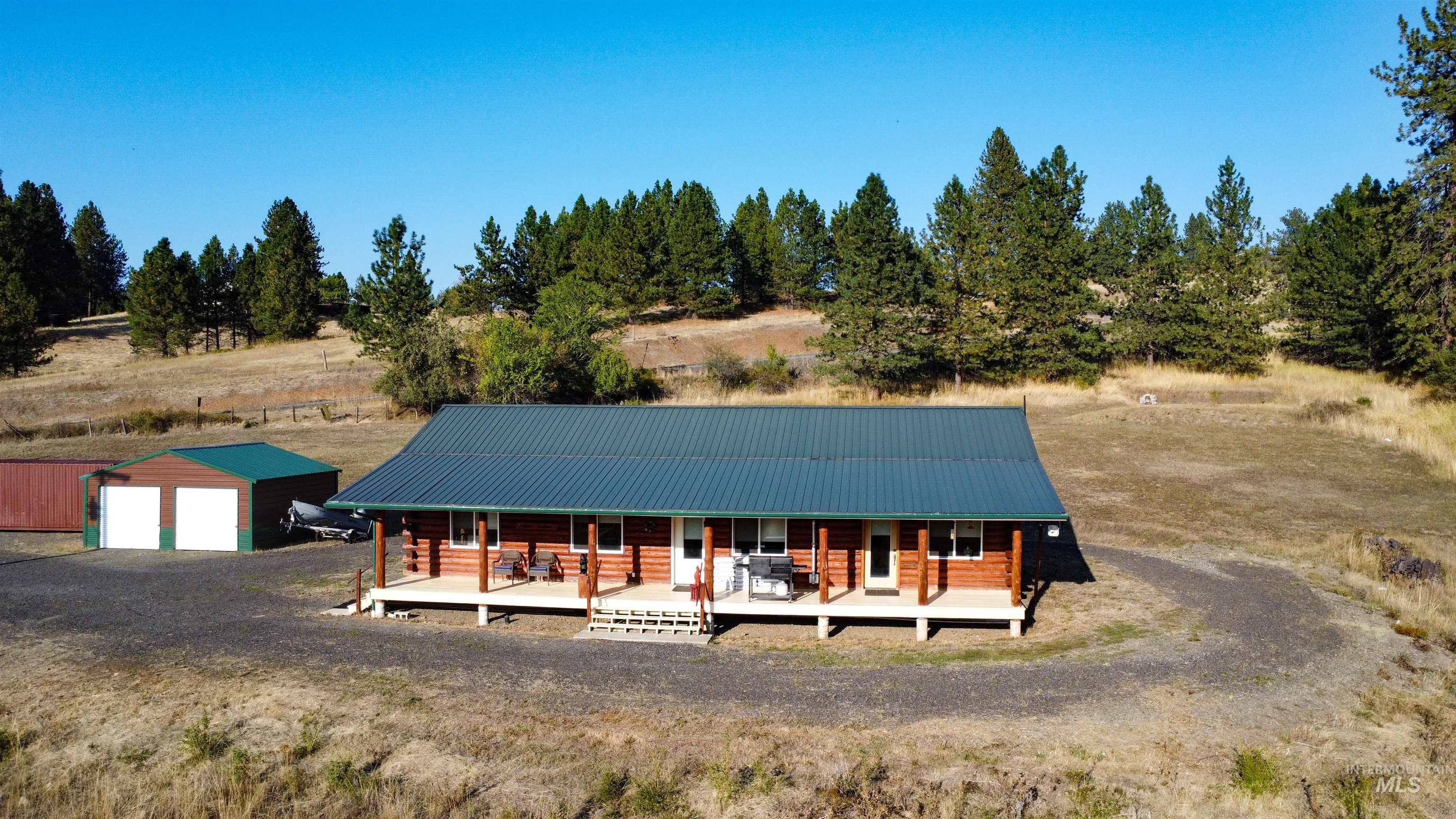 Log-style house with a porch, an outbuilding, a metal roof, a garage, and view of wooded area