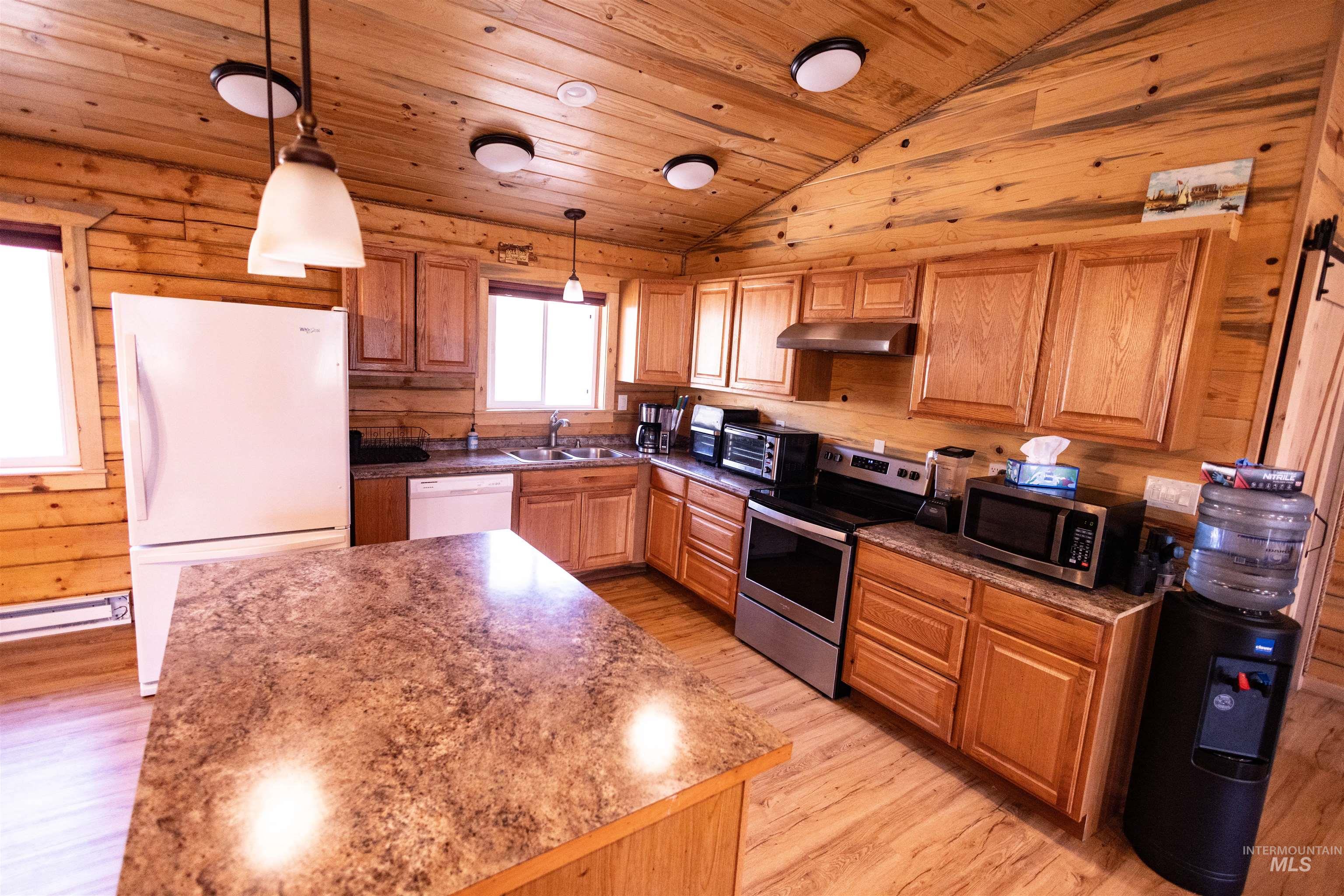 Kitchen with wooden walls, wood ceiling, light wood finished floors, stainless steel appliances, and brown cabinets