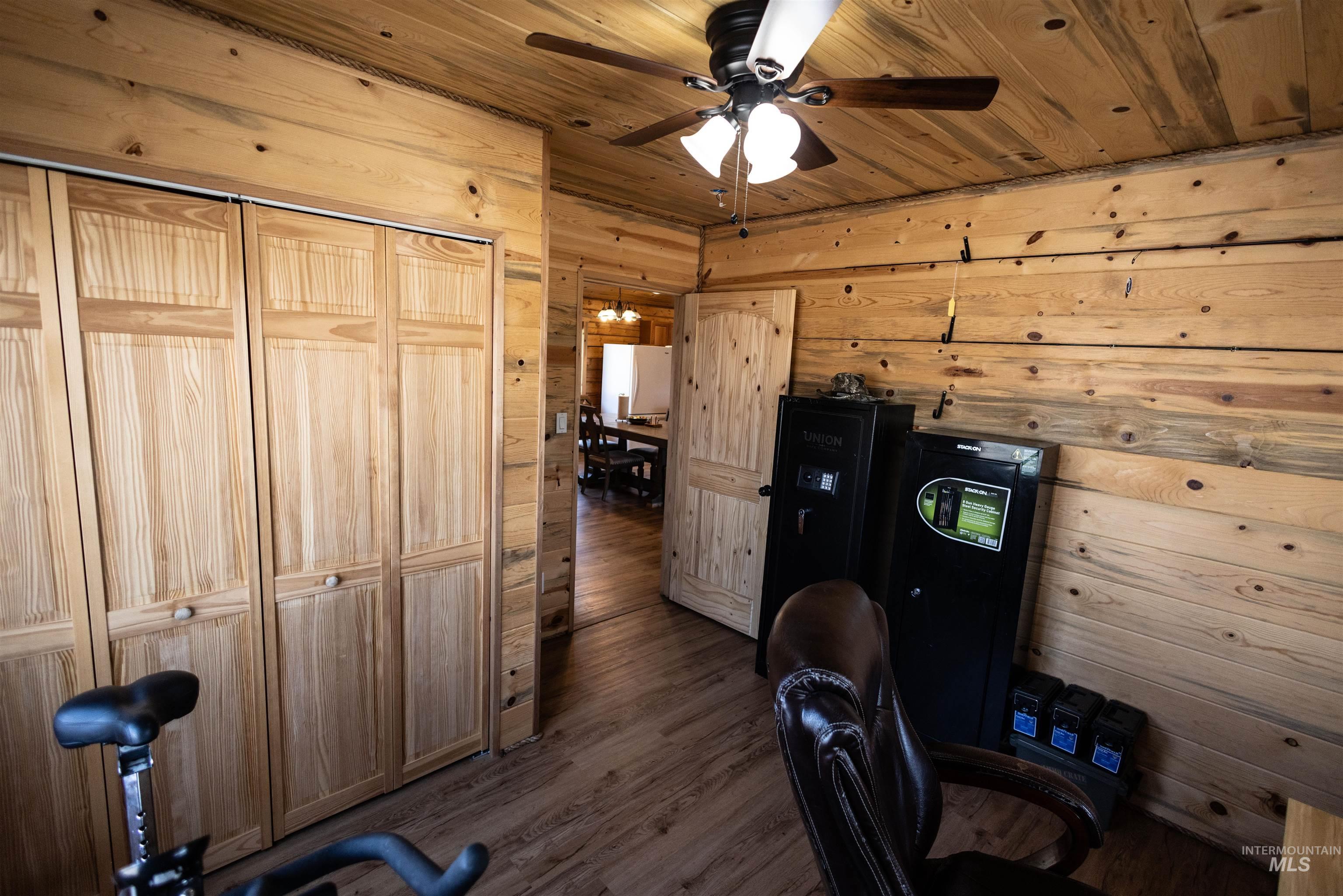 Home office featuring wood walls, wooden ceiling, dark wood-type flooring, and a ceiling fan