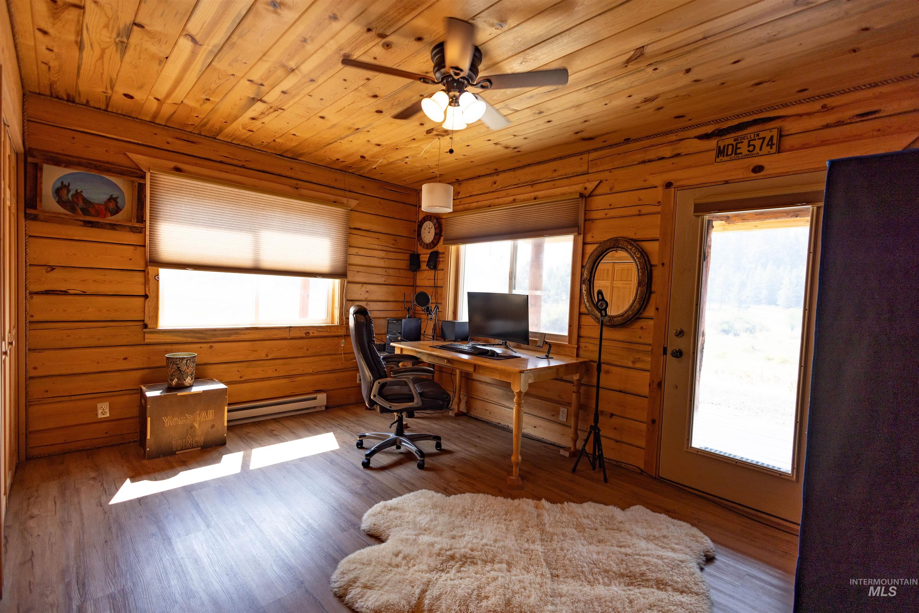 Office area featuring wood ceiling, wood finished floors, a baseboard heating unit, ceiling fan, and wooden walls