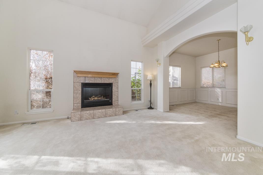 Unfurnished living room with carpet floors, high vaulted ceiling, a tiled fireplace, a chandelier, and arched walkways