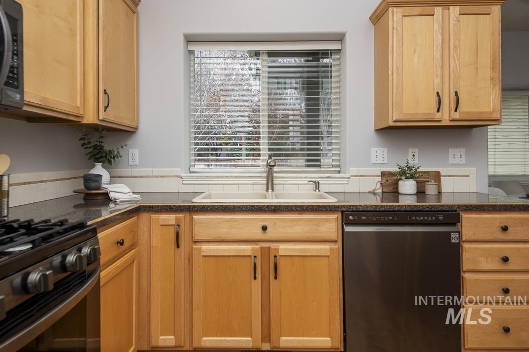 Kitchen with dishwashing machine, black microwave, range with gas stovetop, light brown cabinetry, and dark stone countertops