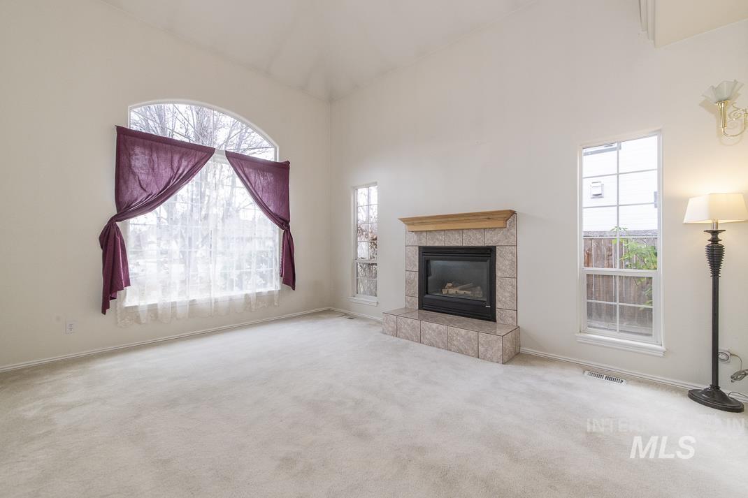 Unfurnished living room featuring a high ceiling, carpet, plenty of natural light, and a tiled fireplace