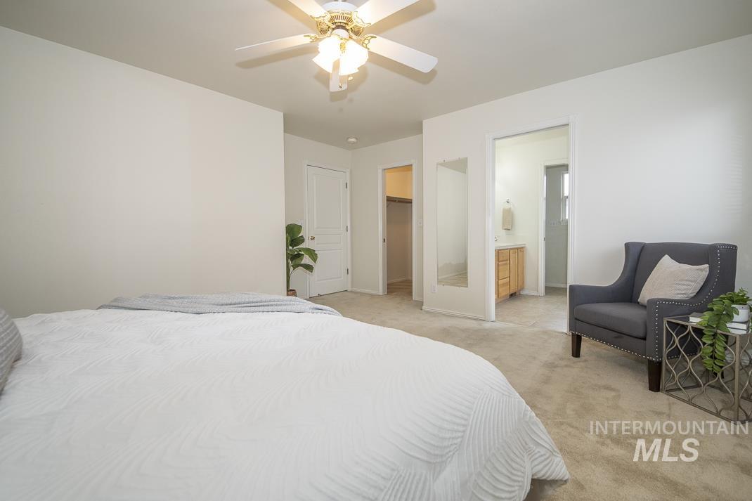 Carpeted bedroom with a walk in closet, ceiling fan, and ensuite bath