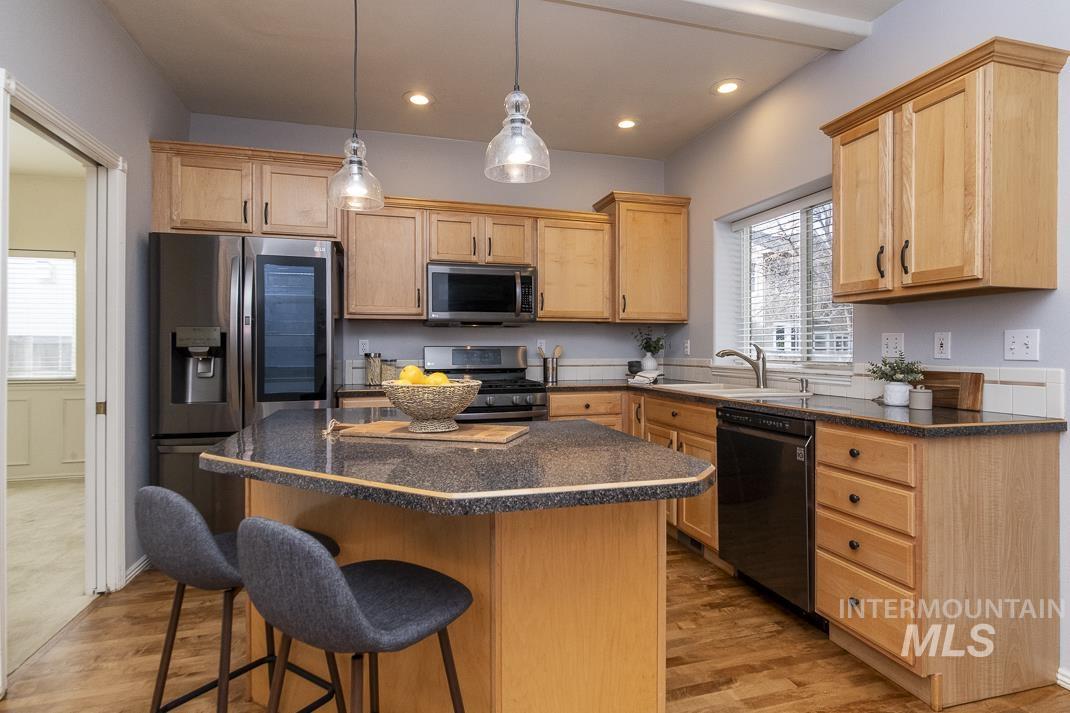 Kitchen featuring a center island, light brown cabinets, stainless steel appliances, decorative light fixtures, and dark stone counters