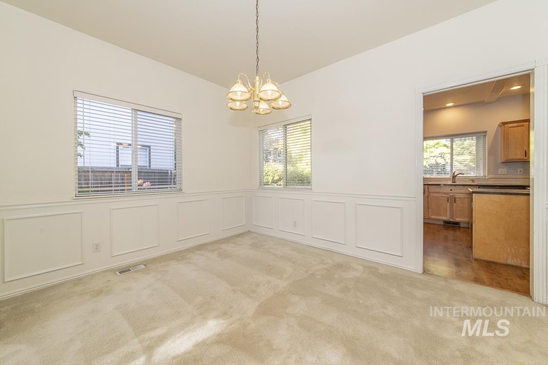 Unfurnished dining area with a decorative wall, wainscoting, a chandelier, and light carpet