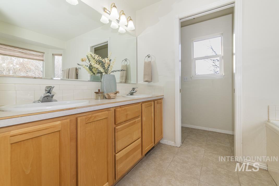 Full bath featuring double vanity, plenty of natural light, tasteful backsplash, and light tile patterned floors