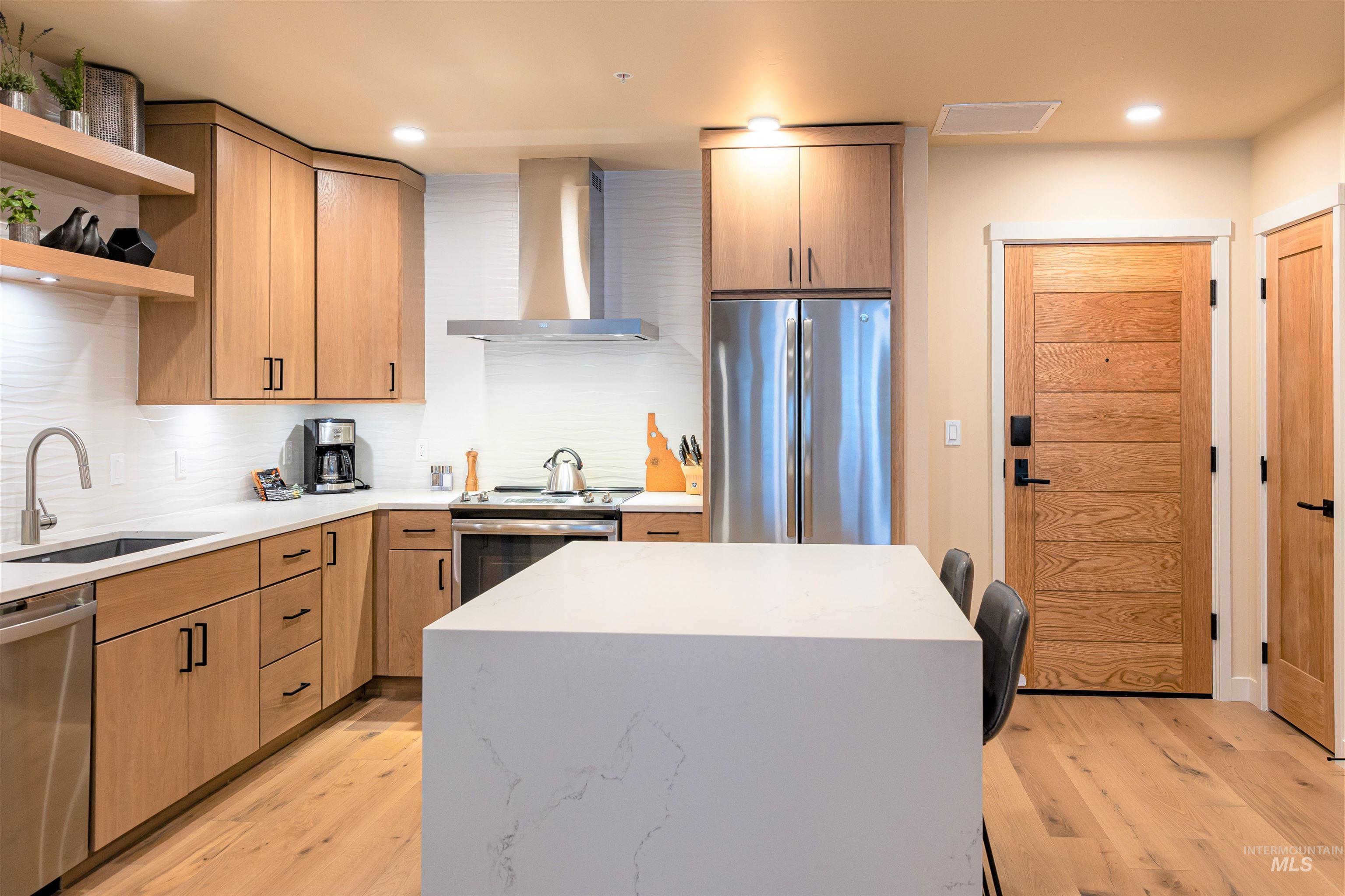 Kitchen with open shelves, stainless steel appliances, wall chimney exhaust hood, light stone counters, and light wood-style flooring
