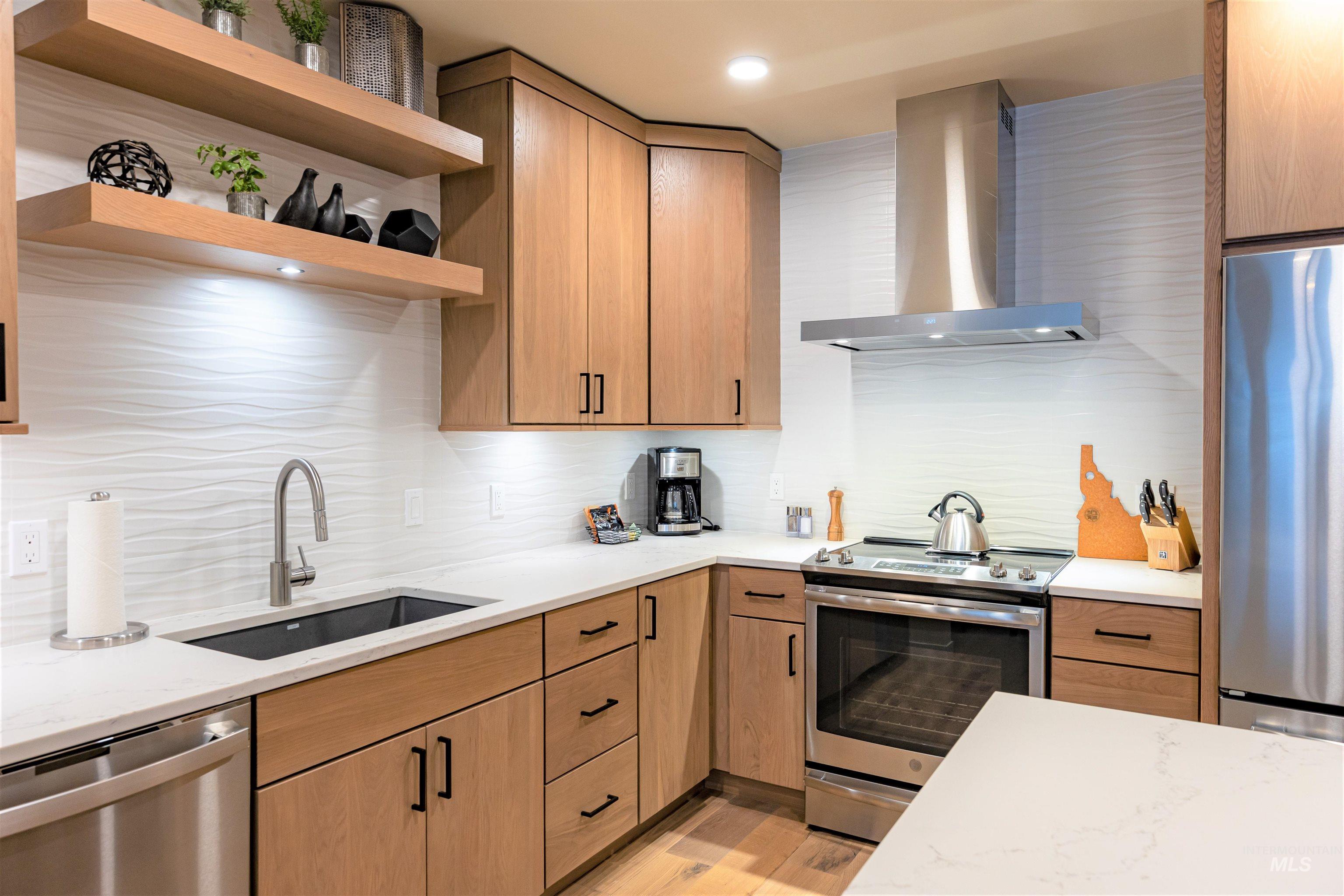 Kitchen with stainless steel appliances, wall chimney exhaust hood, open shelves, tasteful backsplash, and light stone countertops