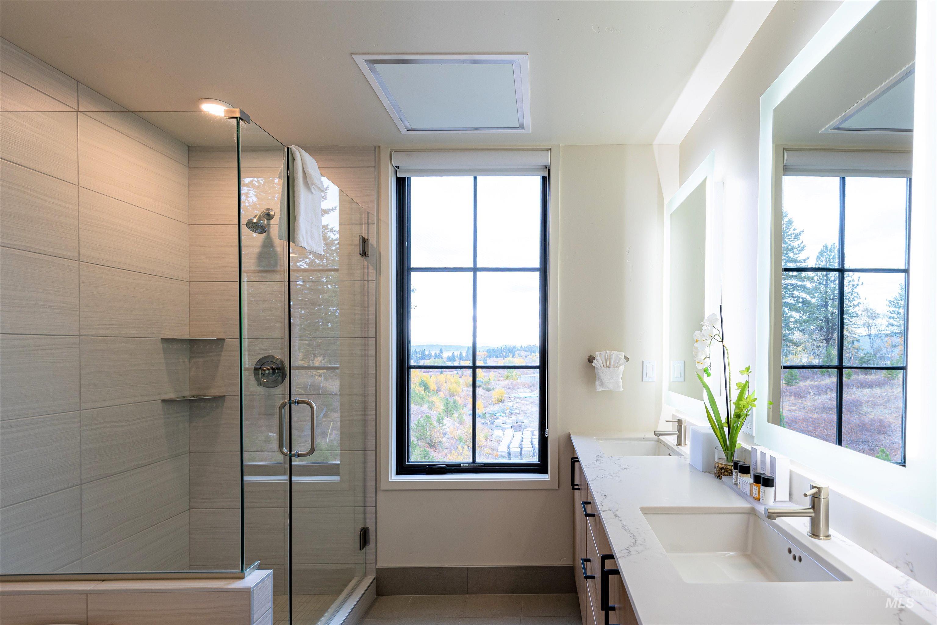 Bathroom with double vanity, a shower stall, tile patterned floors, and plenty of natural light