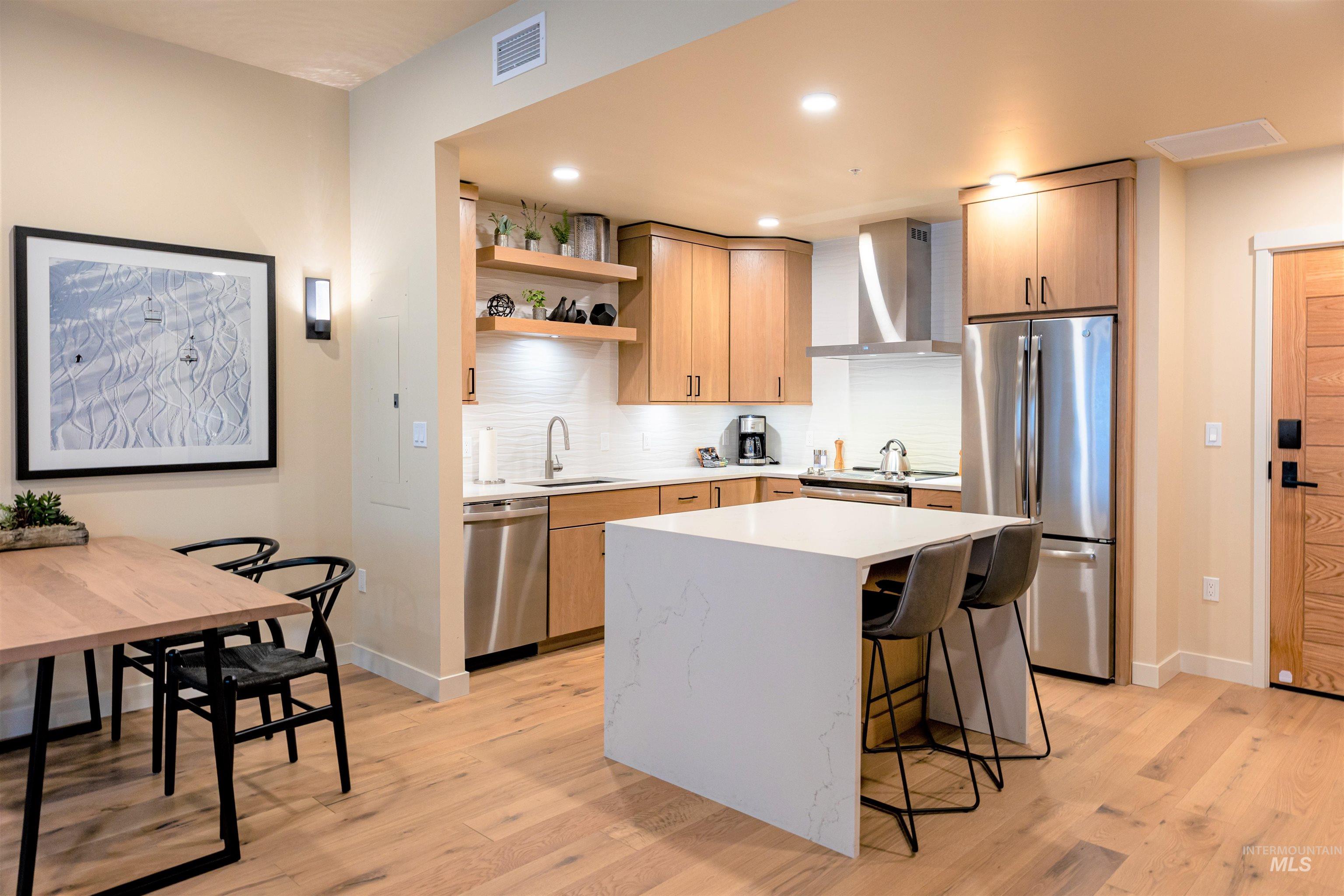 Kitchen with backsplash, a kitchen bar, appliances with stainless steel finishes, light stone countertops, and open shelves