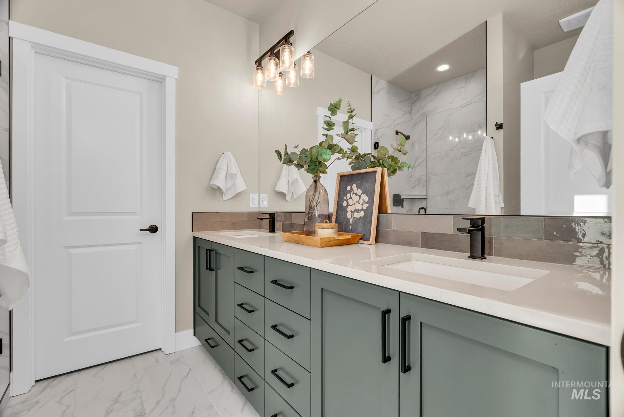 Bathroom with double vanity, light marble finish floors, and a marble finish shower