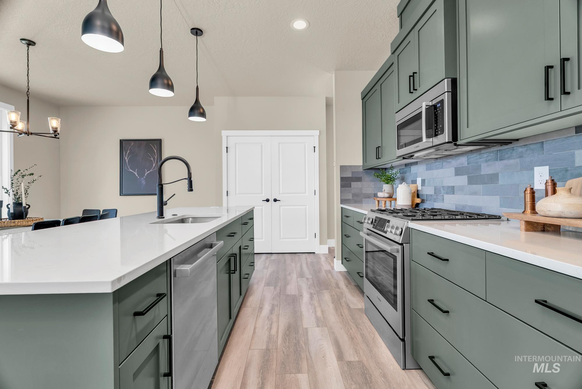 Kitchen featuring green cabinets, appliances with stainless steel finishes, hanging light fixtures, light wood-type flooring, and tasteful backsplash