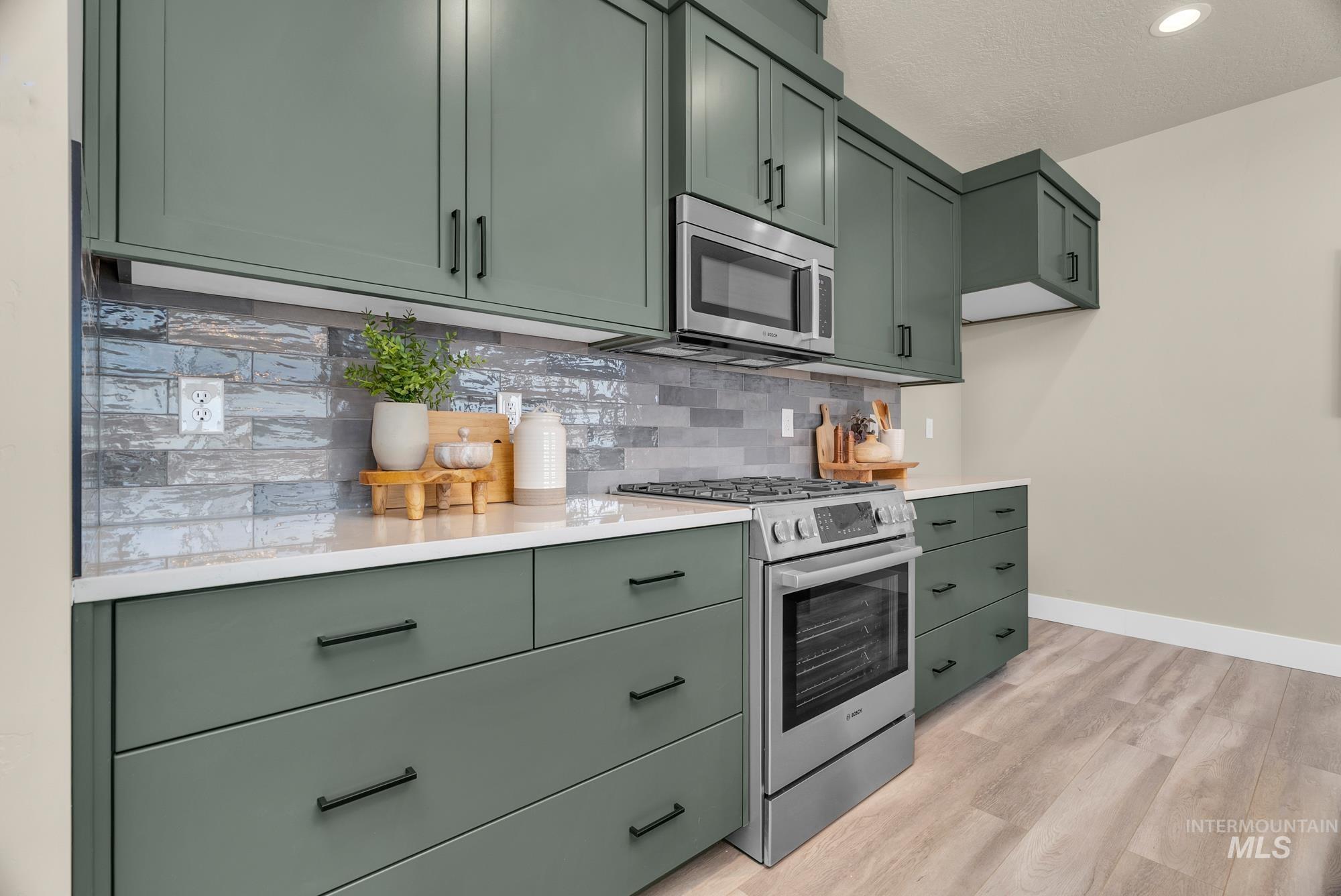 Kitchen with green cabinets, appliances with stainless steel finishes, tasteful backsplash, light wood-type flooring, and a textured ceiling