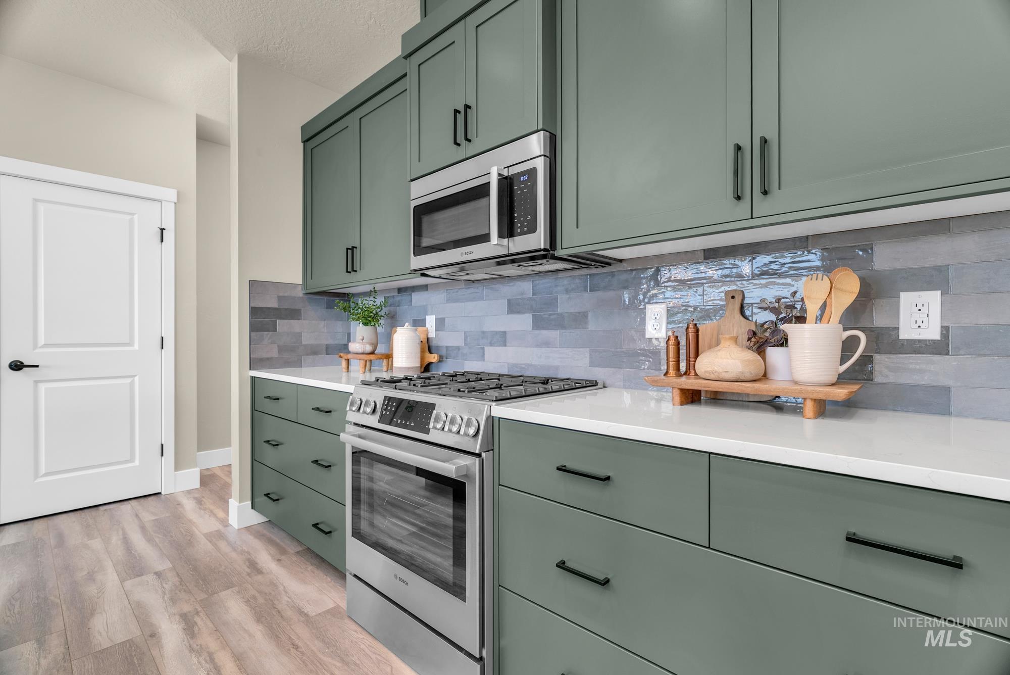 Kitchen with green cabinetry, appliances with stainless steel finishes, backsplash, light wood finished floors, and a textured ceiling