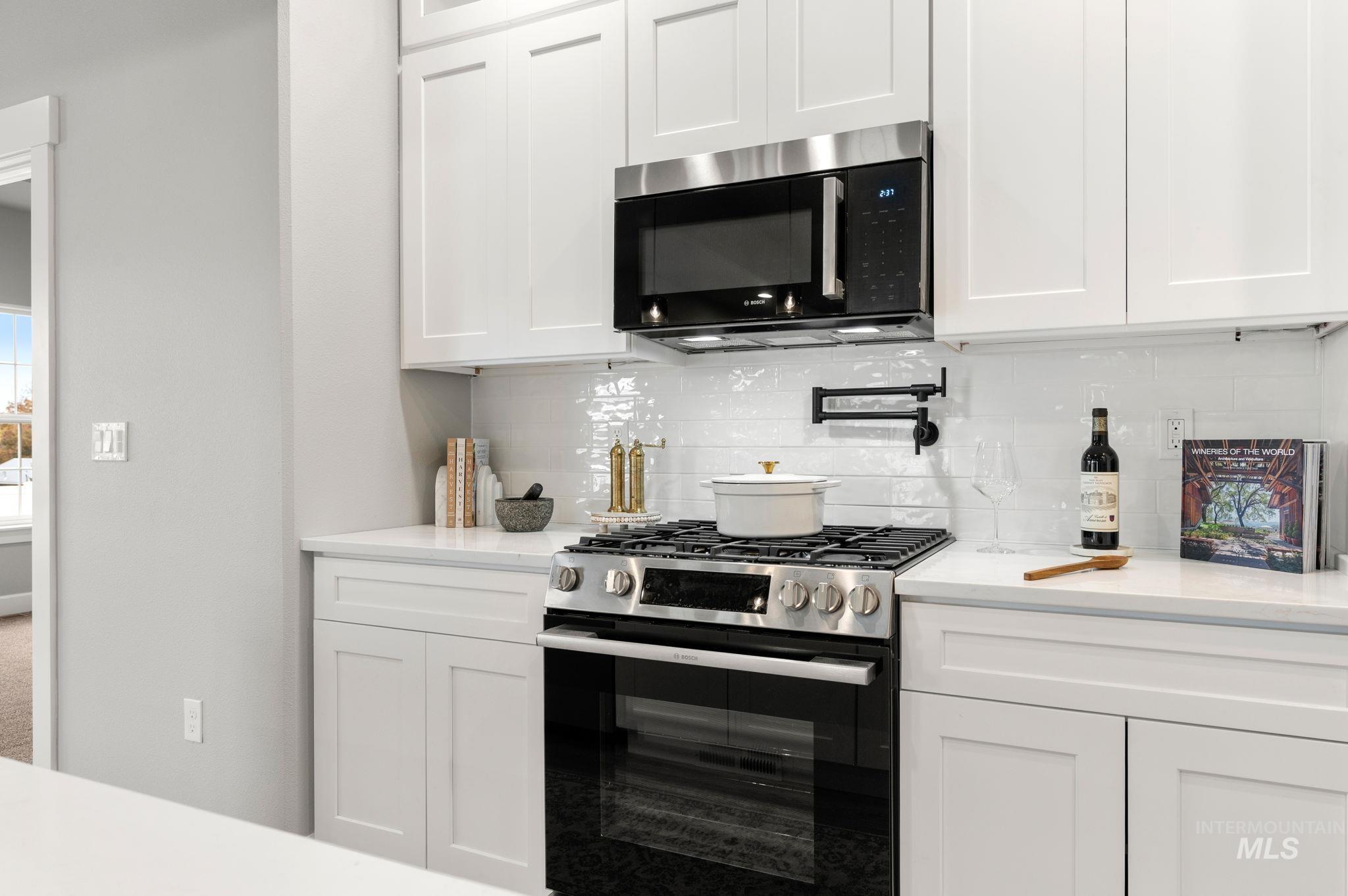 Kitchen with stainless steel range with gas cooktop, white cabinets, black microwave, and decorative backsplash