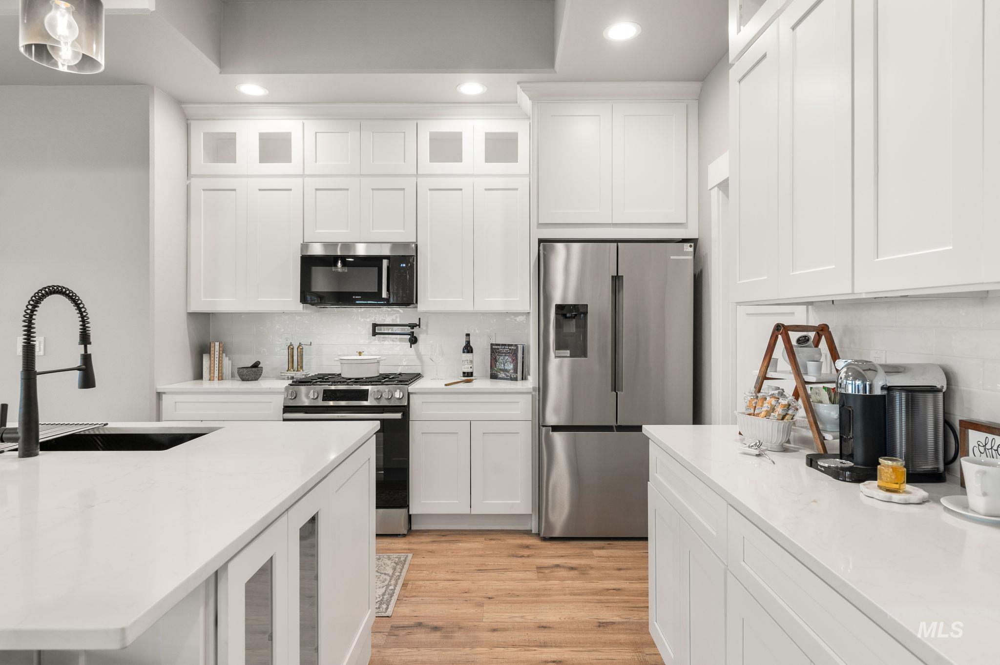 Kitchen with glass insert cabinets, stainless steel appliances, recessed lighting, light wood finished floors, and white cabinets