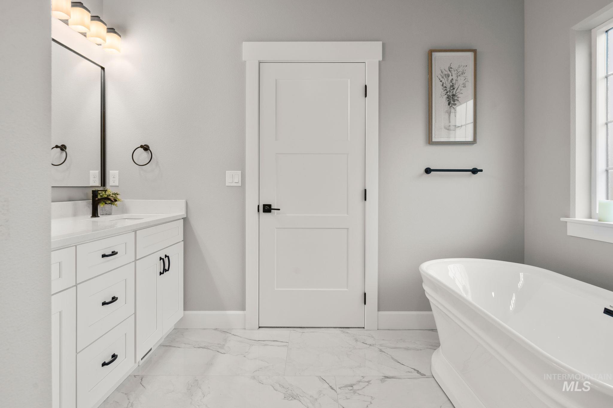 Bathroom featuring a freestanding bath, light marble style tiled floors, and vanity