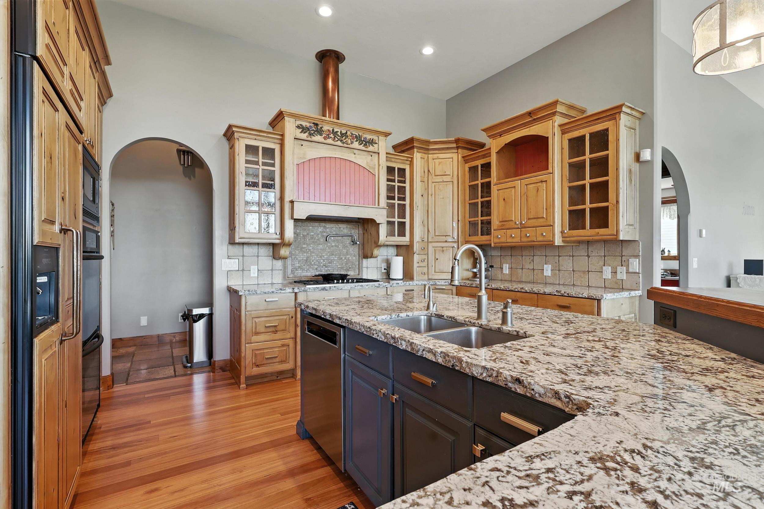 Kitchen featuring arched walkways, glass insert cabinets, light wood-style flooring, tasteful backsplash, and recessed lighting
