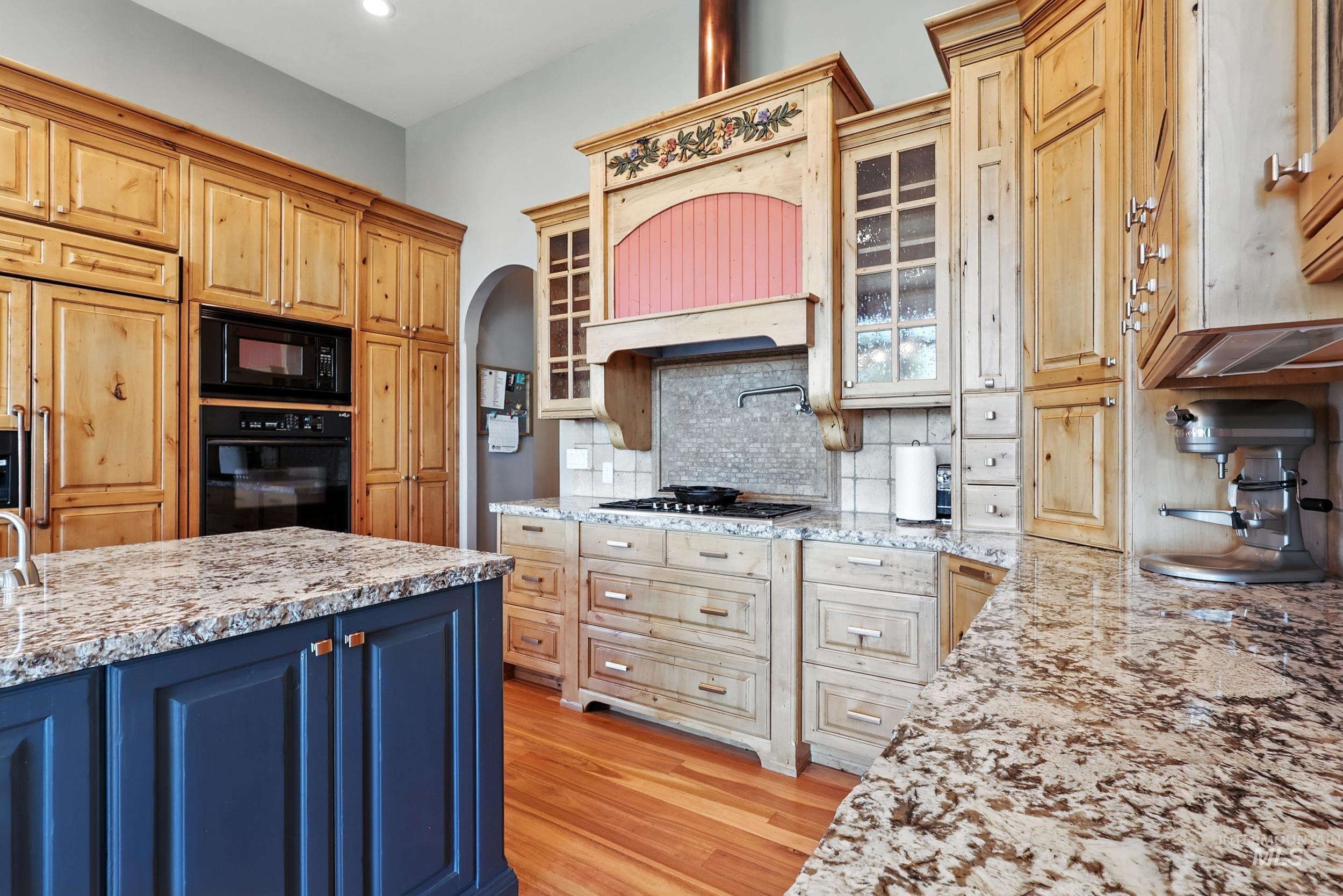 Kitchen featuring blue cabinets, glass insert cabinets, tasteful backsplash, black appliances, and light wood-type flooring