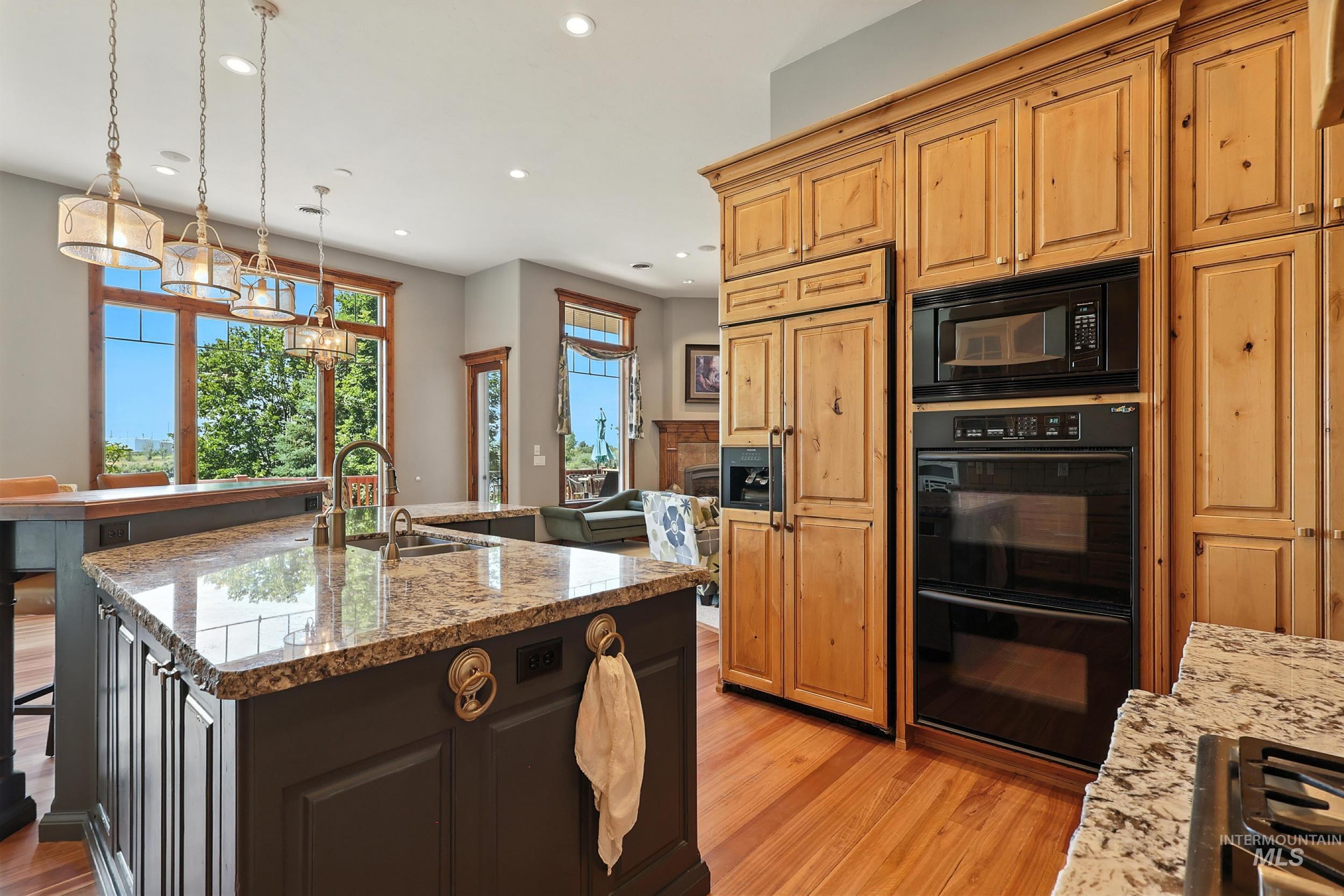 Kitchen featuring black appliances, hanging light fixtures, light stone countertops, light wood-type flooring, and recessed lighting