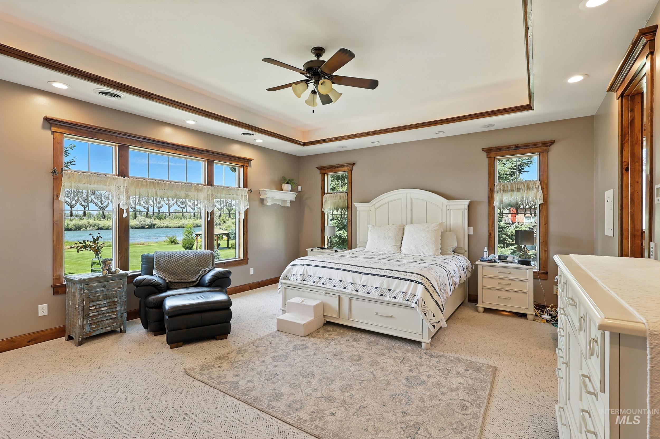Bedroom with a water view, a ceiling fan, light colored carpet, recessed lighting, and a tray ceiling