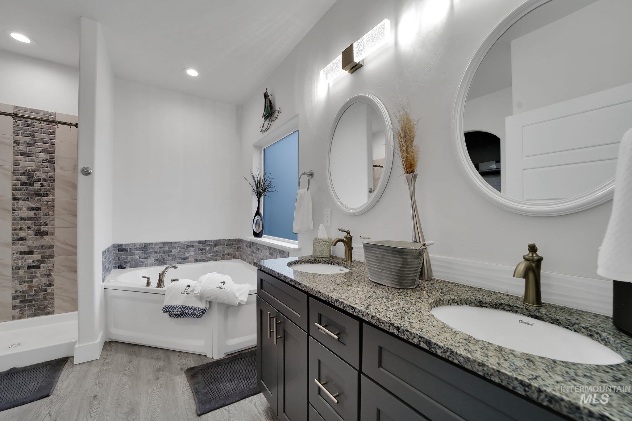 Full bath featuring a garden tub, double vanity, light wood-style floors, tiled shower, and recessed lighting