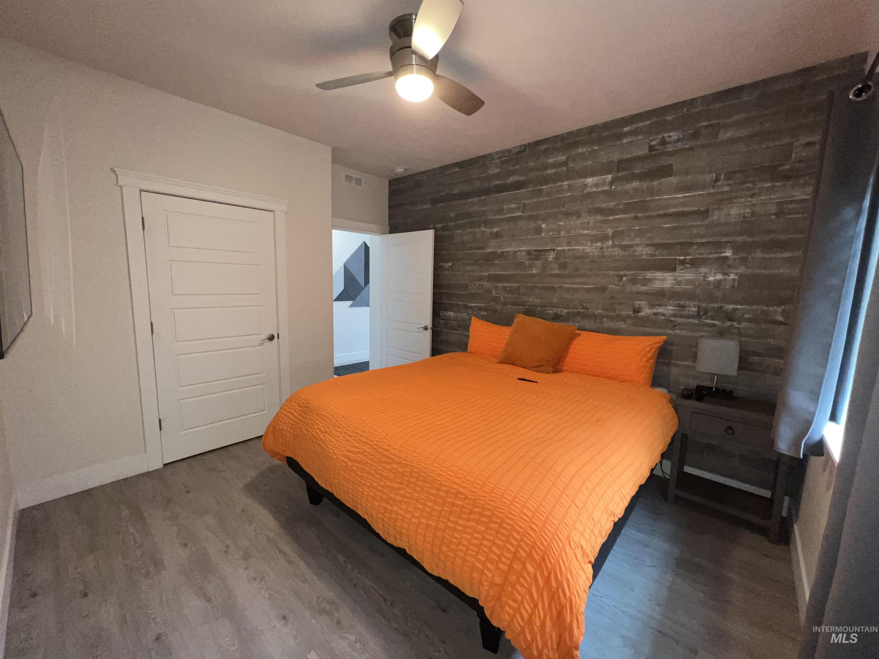 Bedroom featuring an accent wall, wooden walls, wood finished floors, and a ceiling fan