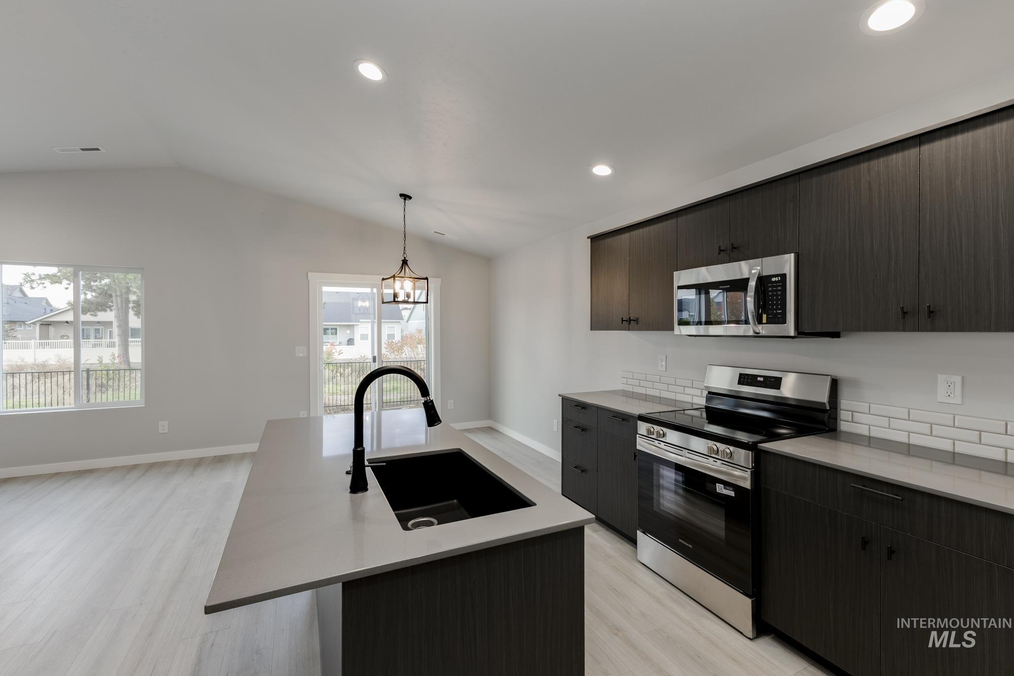 Kitchen featuring stainless steel appliances, modern cabinets, light wood-style flooring, decorative light fixtures, and lofted ceiling